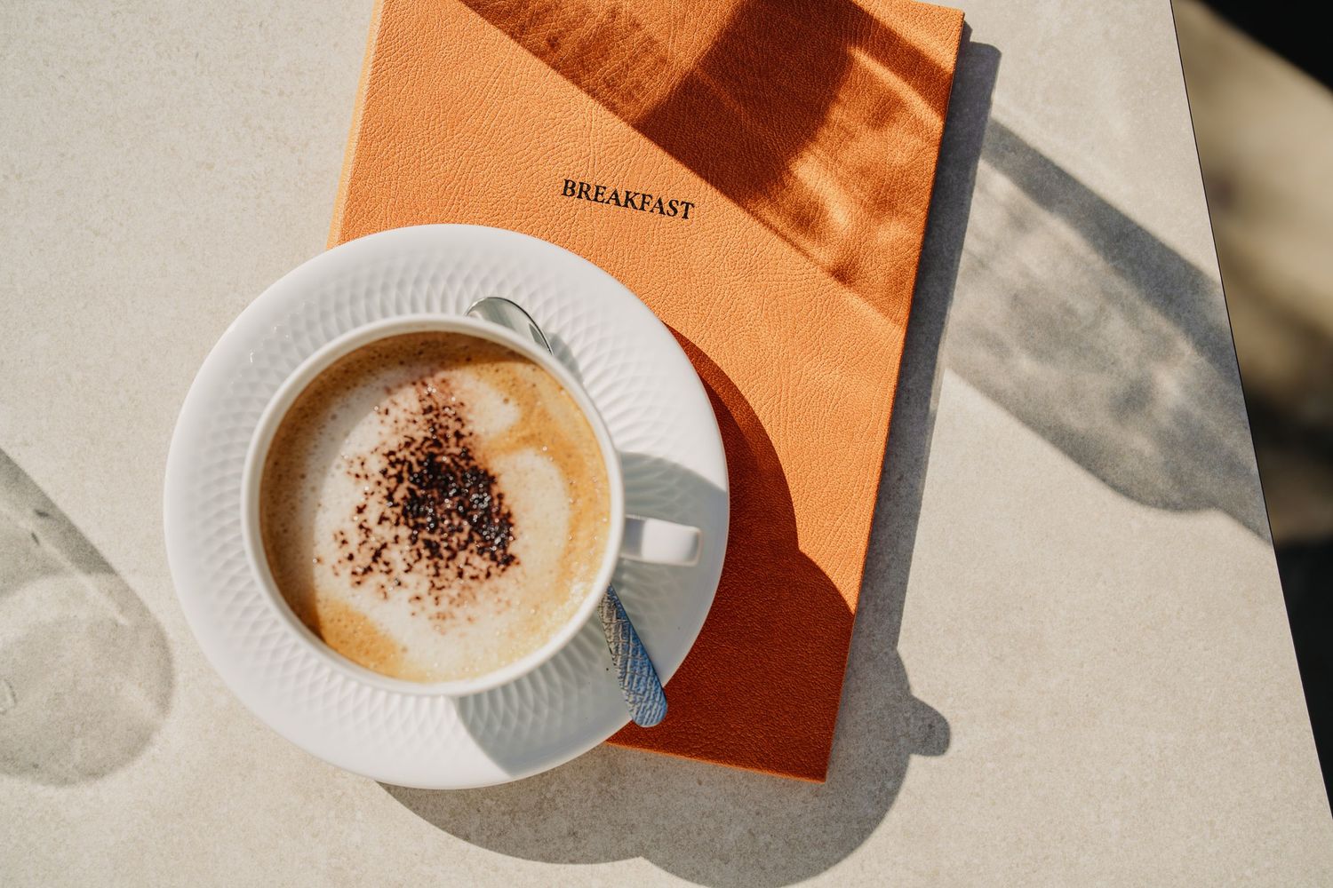 Overhead view of coffee cups with latte art casting shadows on a light colored surface in warm morning light.