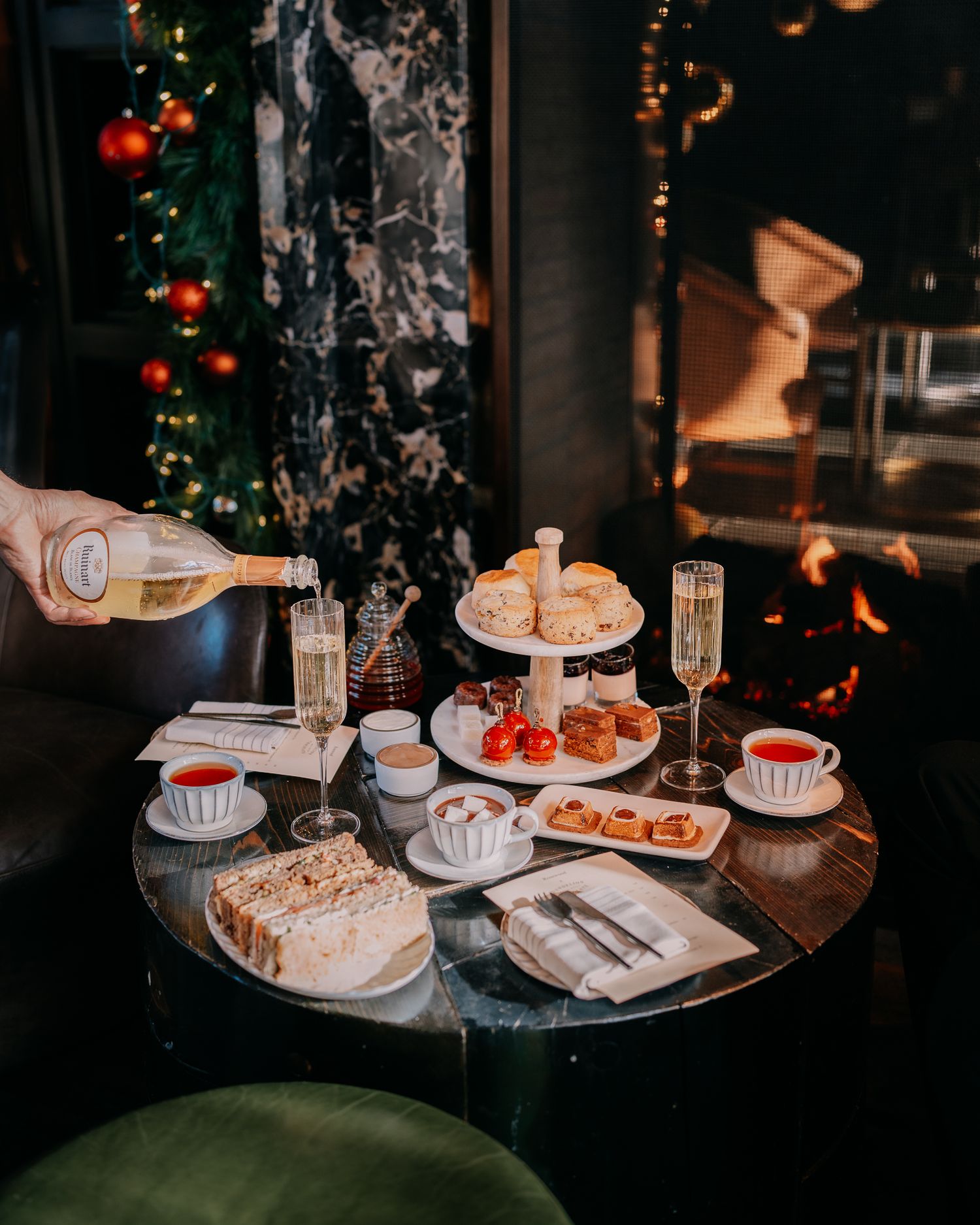 Festive holiday spread with champagne, pastries, and tea service against Christmas tree backdrop.