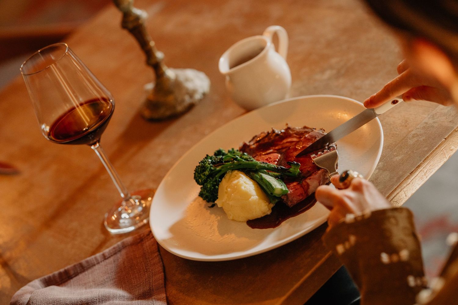 Fine dining table with plated dishes, wine glasses, and cups in warm lighting.