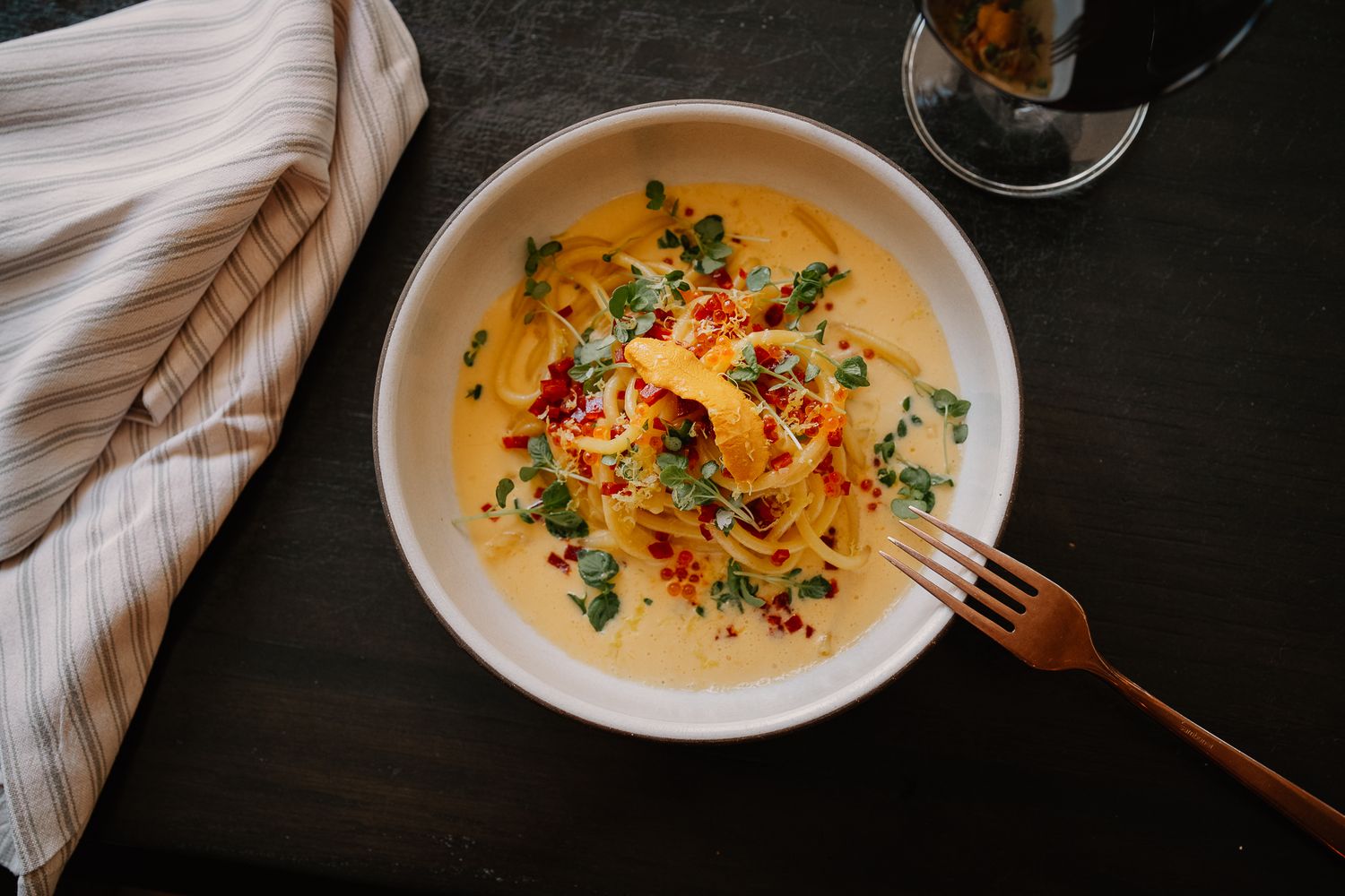 A bowl of creamy pasta garnished with fresh herbs and red pepper flakes served with a copper fork.