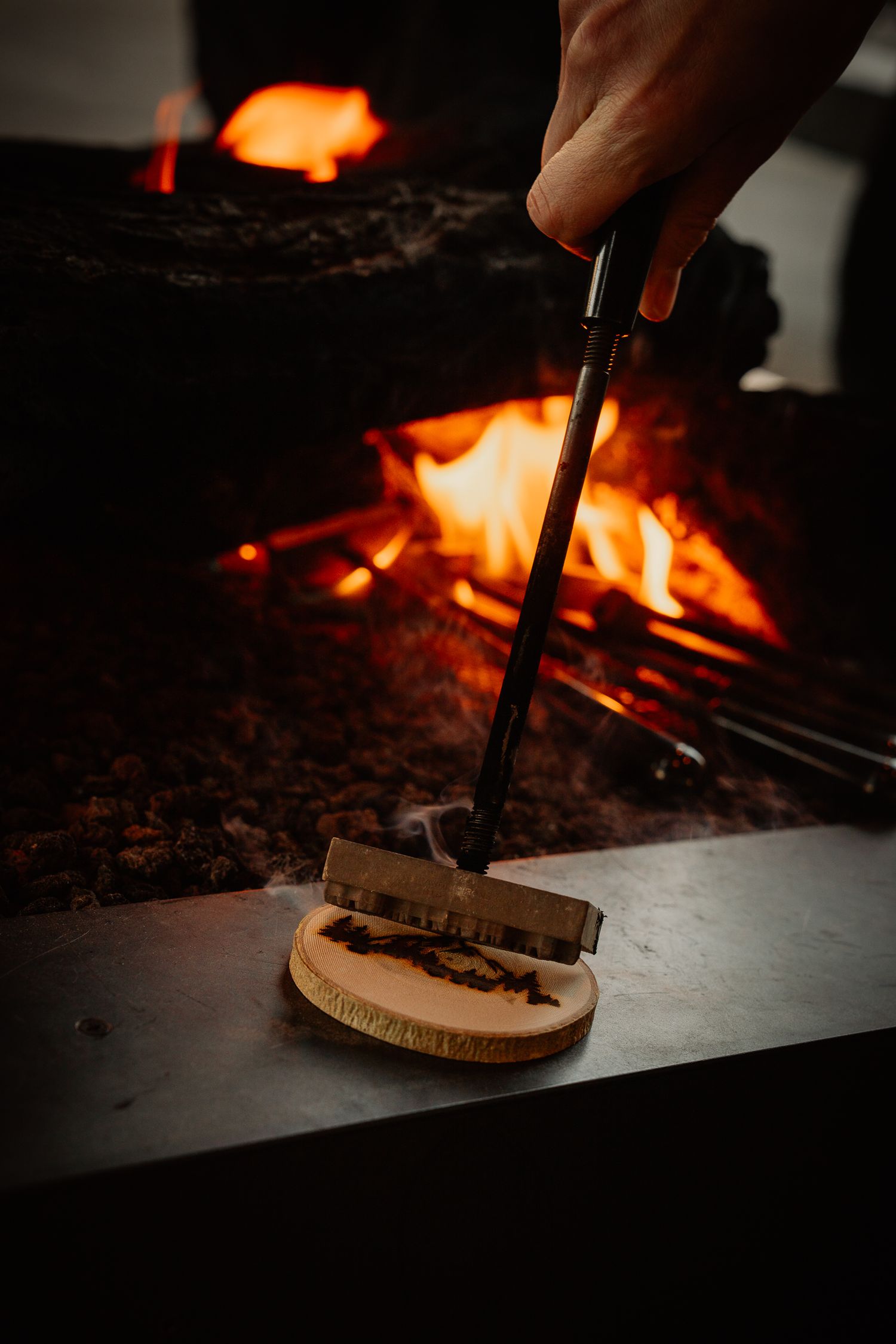 Close-up of hands grilling mushrooms over an open flame with dramatic lighting.