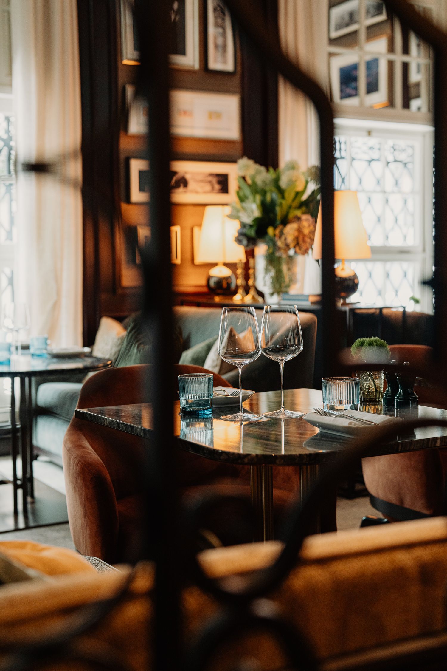 Elegant restaurant dining area with plush seating and decorative window panels in warm atmospheric lighting.
