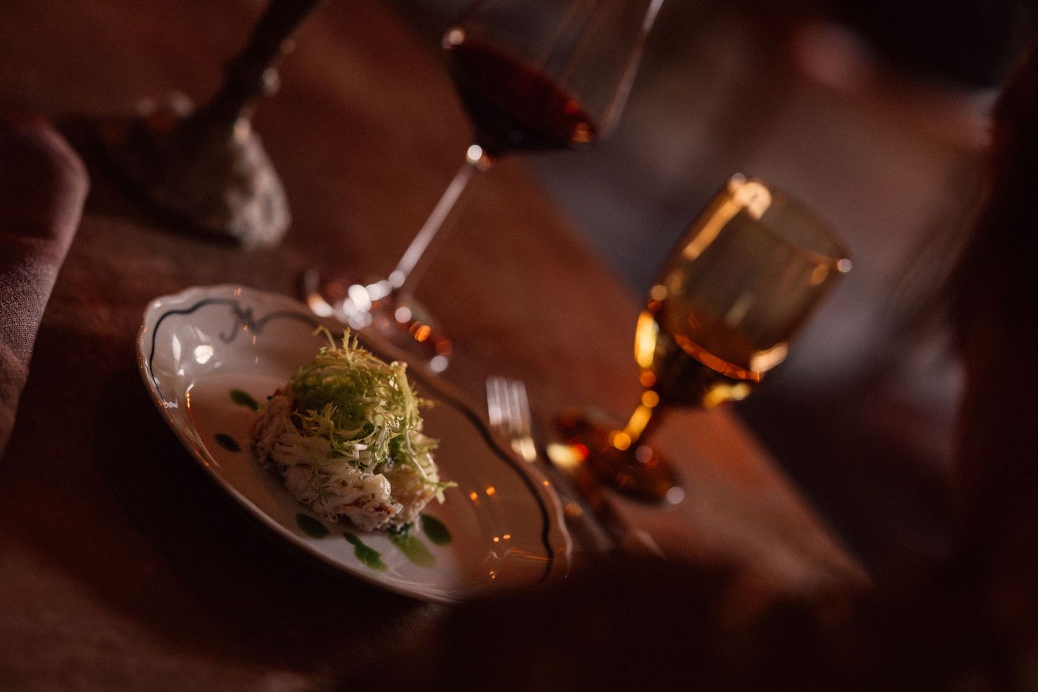 A collection of wine glasses in various stages of being filled with red wine in a dimly lit setting.