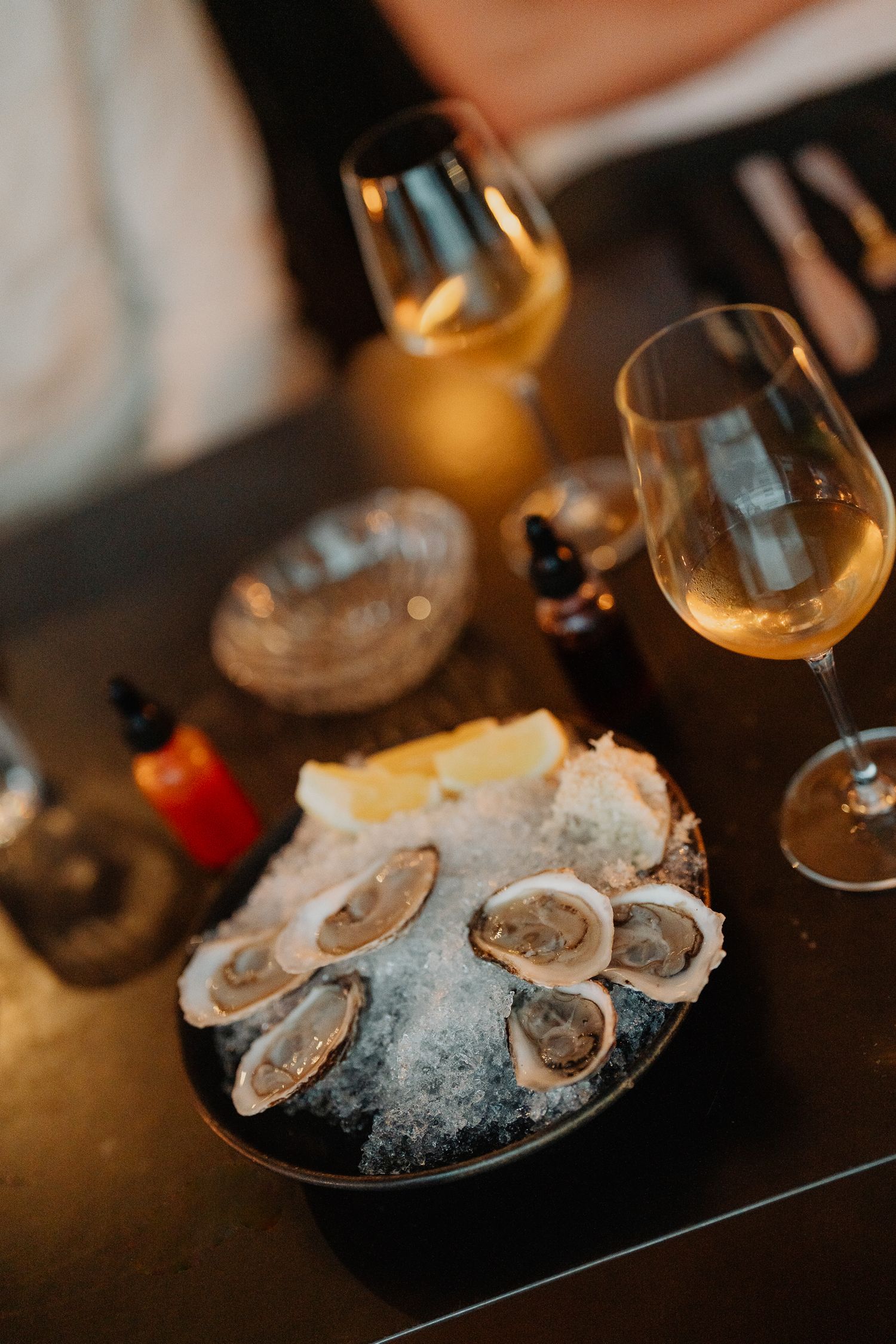Fresh oysters on ice served with white wine glasses and accompaniments in an elegant dining setting.