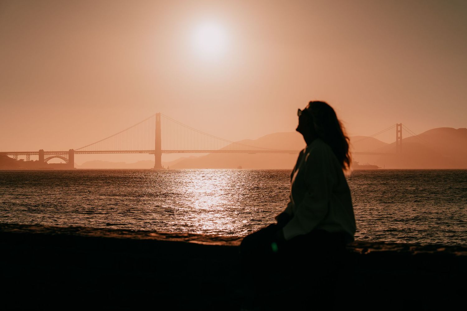 Silhouette of a person watching sunset over San Francisco Bay with Golden Gate Bridge in the distance.