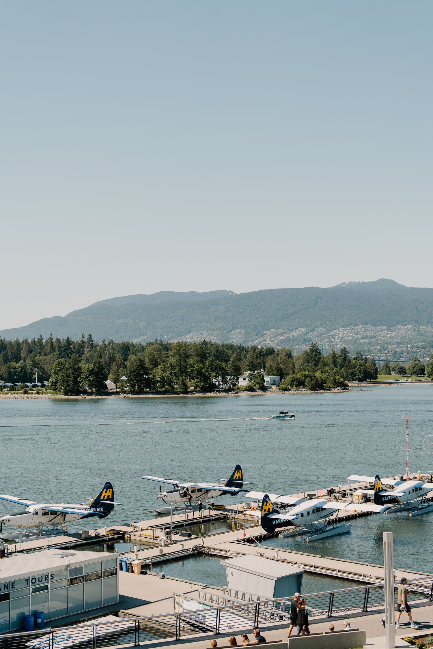 Seaplanes and boats dock at a harbor with mountains and forests in the background along Vancouver's coastline.