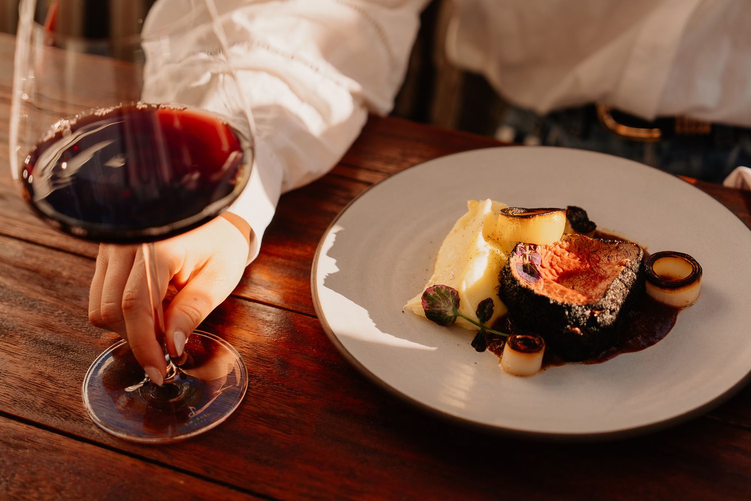 Elegant fine dining plate with gourmet dish beside a glass of red wine on a rustic wooden table.
