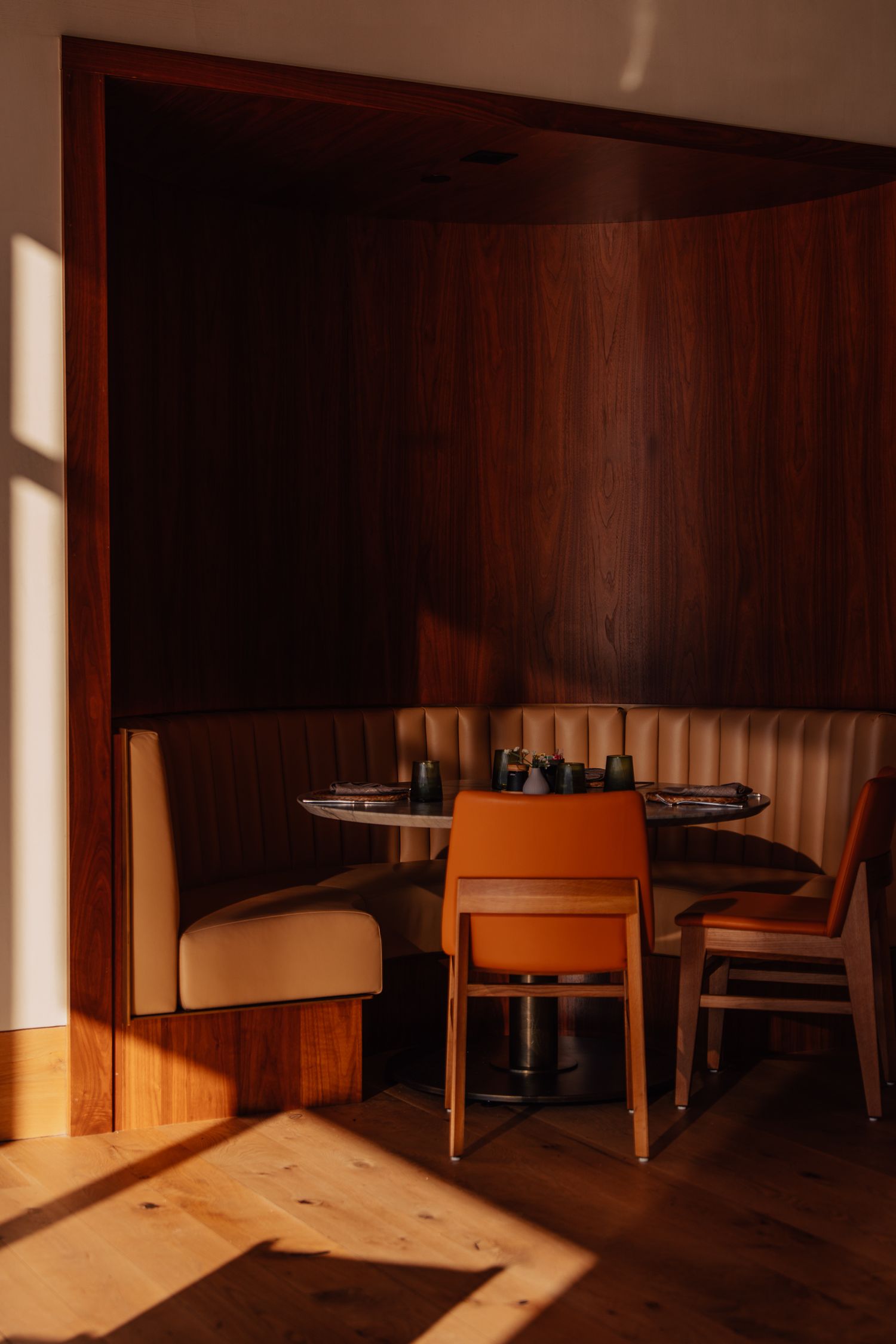 Sunlight streams through windows into an empty wooden dining room with modern furniture.