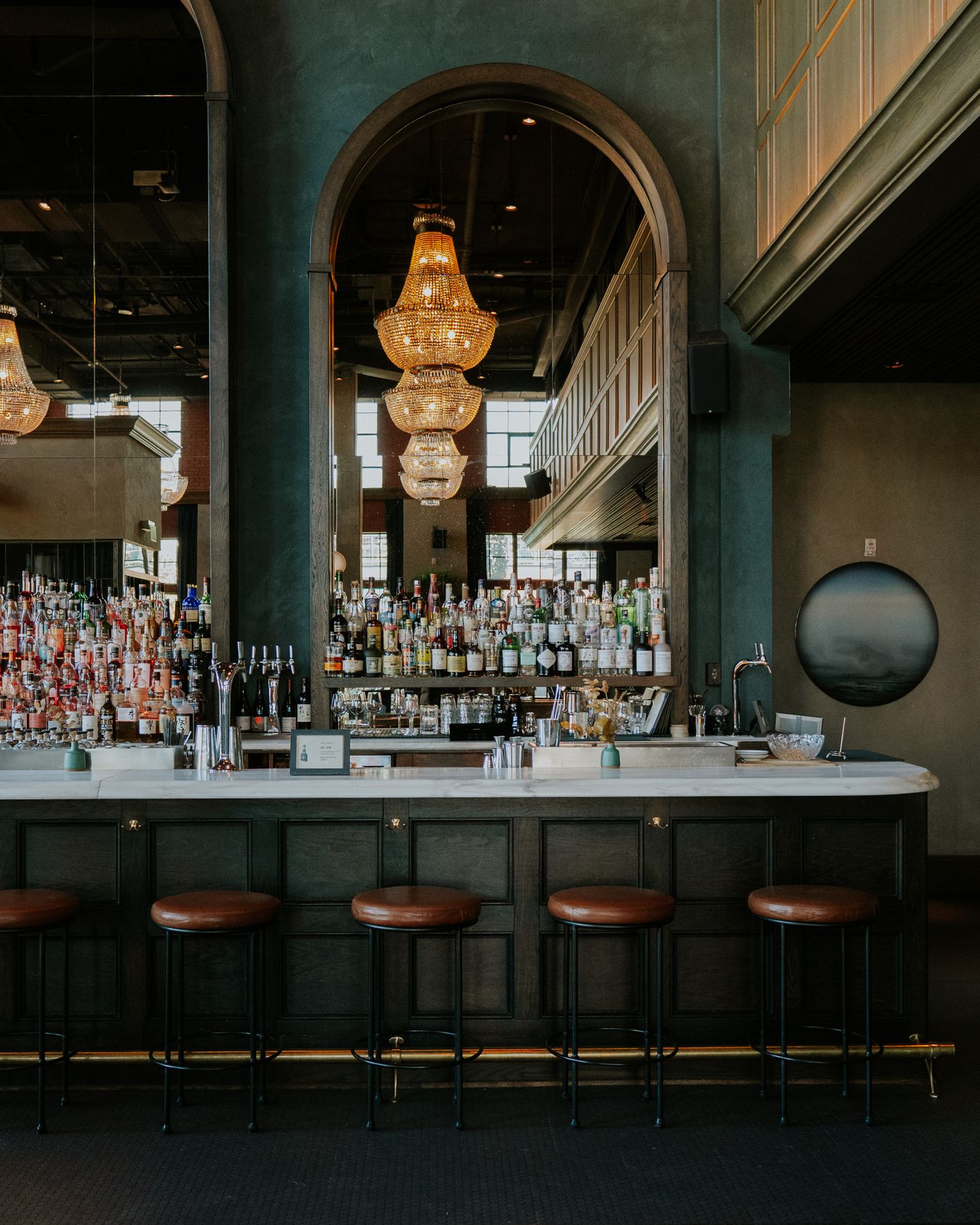 Dark wood bar with modern white countertop and elegant crystal chandelier creates luxurious lounge ambiance.