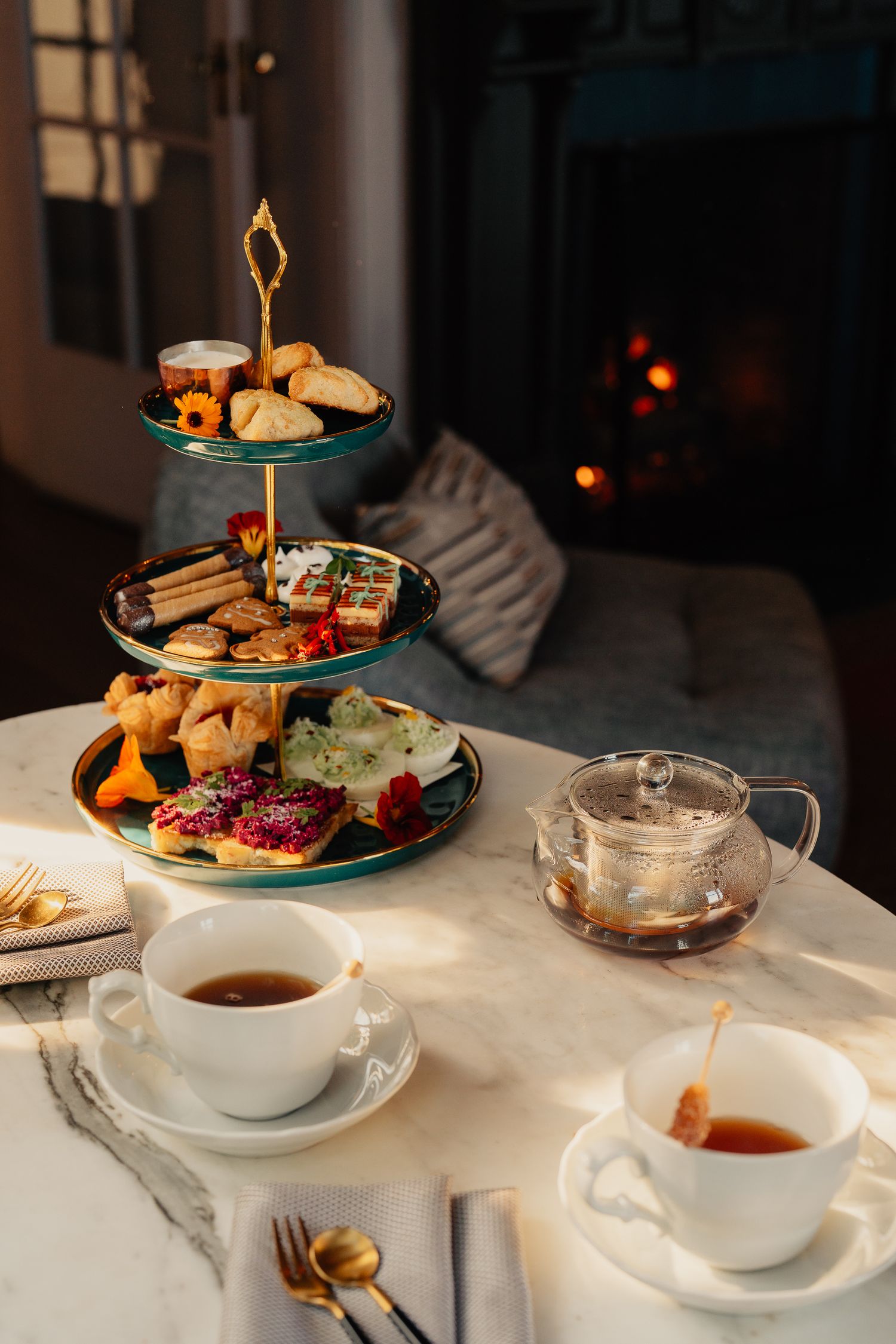 Elegant afternoon tea service with tiered stands of pastries and sandwiches on a white tablecloth in warm lighting.