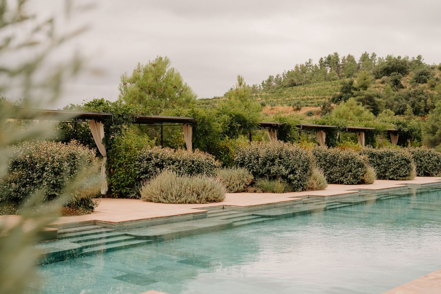 A serene swimming pool surrounded by lush Mediterranean gardens and stone walls in a luxury resort setting.