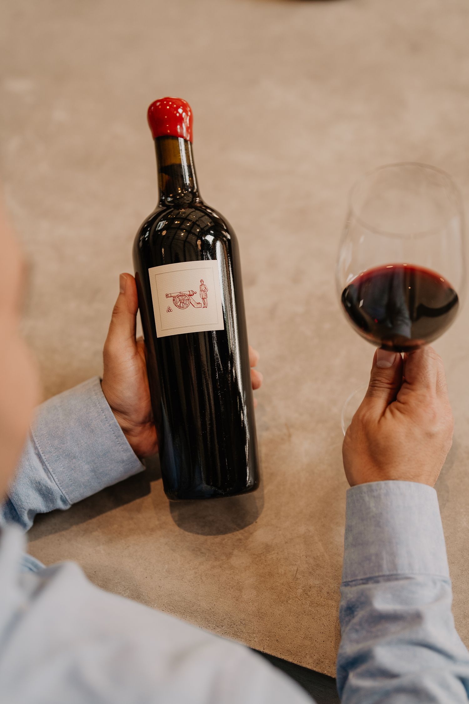 Person holding a bottle of red wine and a glass of red wine at a table.