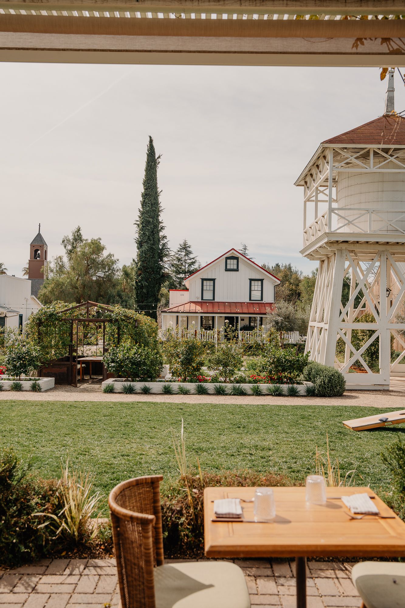 Charming outdoor restaurant patio with garden views, white water tower, and historic farmhouse.