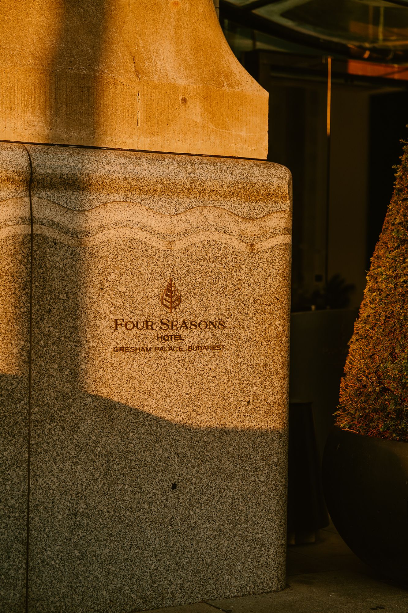Four Seasons Hotel Gresham Palace Budapest sign on granite wall bathed in warm golden sunset light.