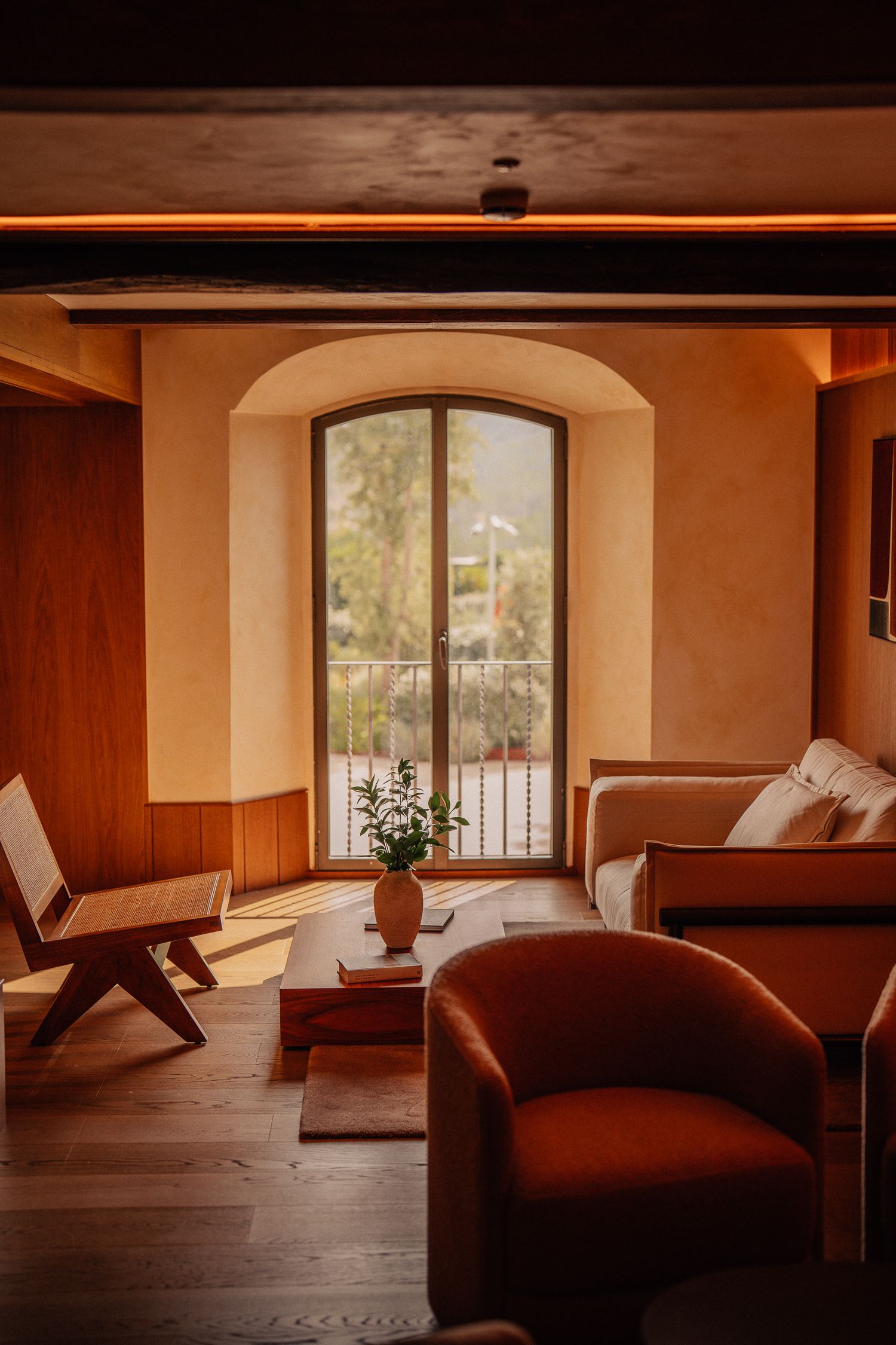 Cozy living room interior with arched window, wooden paneling, and orange armchair in warm evening light.