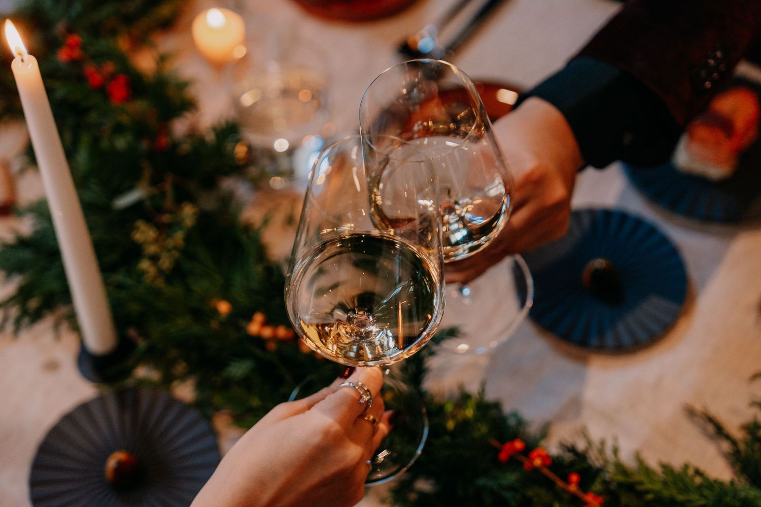 Elegant Christmas table setting with lit candles, wine glasses, and festive decorations glowing in warm light.