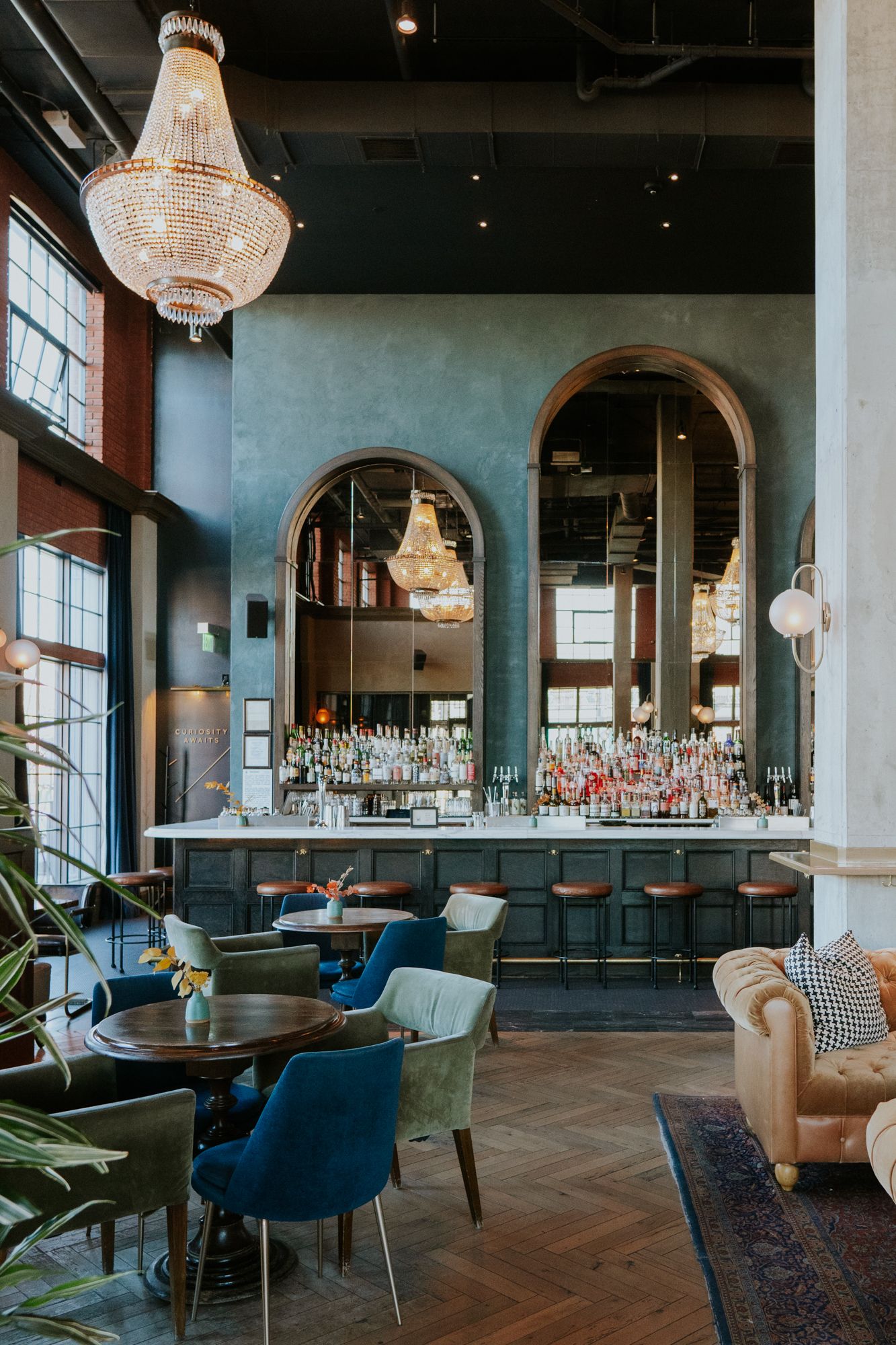 Elegant restaurant interior with crystal chandeliers, blue velvet chairs, and a sophisticated bar area.