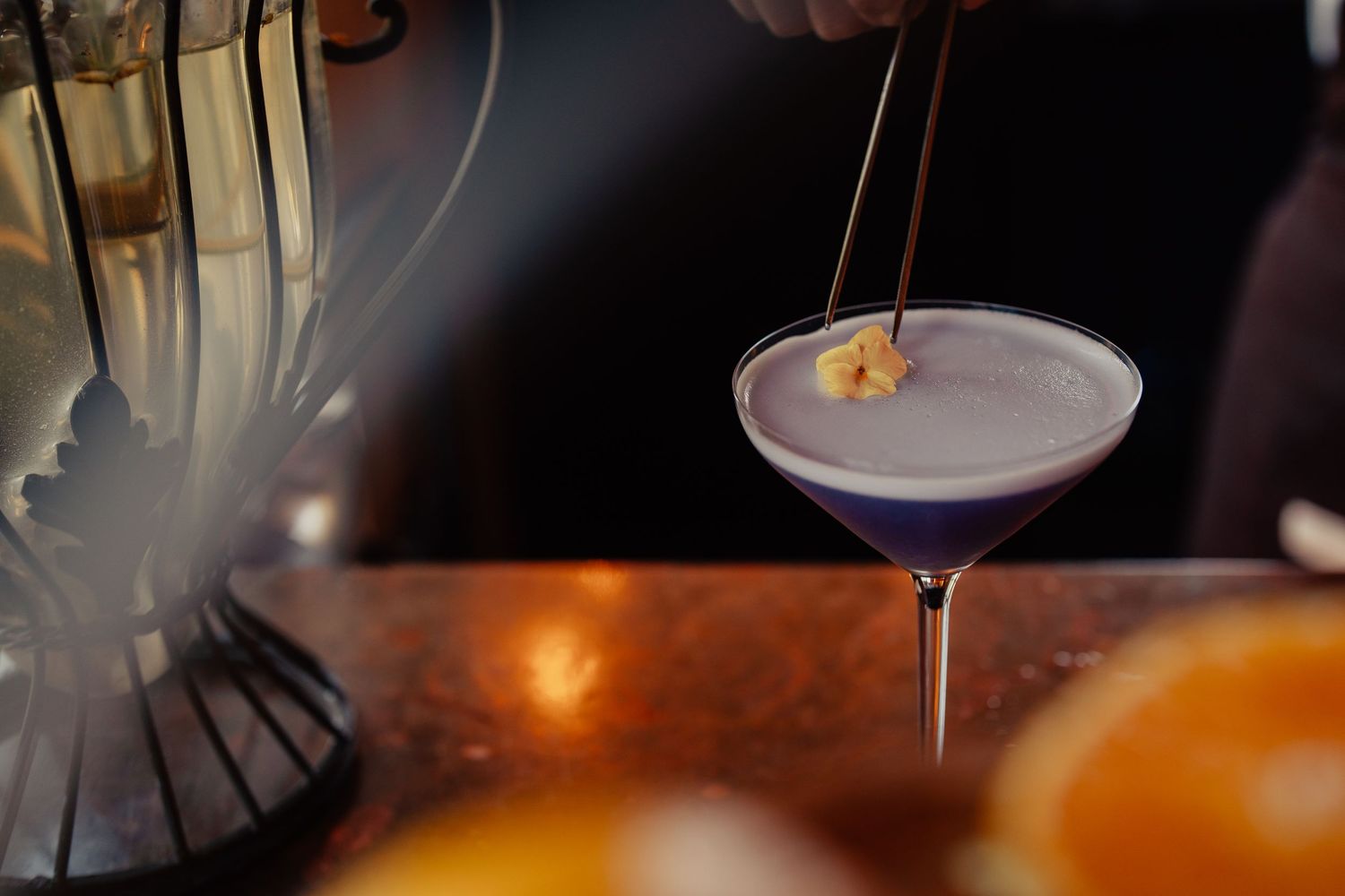 Elegant cocktail glasses filled with colorful drinks sit on a dimly lit bar counter with warm ambient lighting.