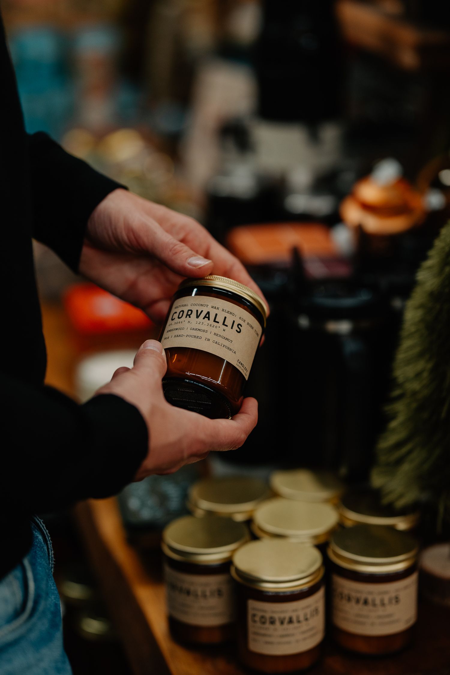 Multiple glass jars of Corvallis branded cosmetic products arranged in a sequence showing hands handling them.