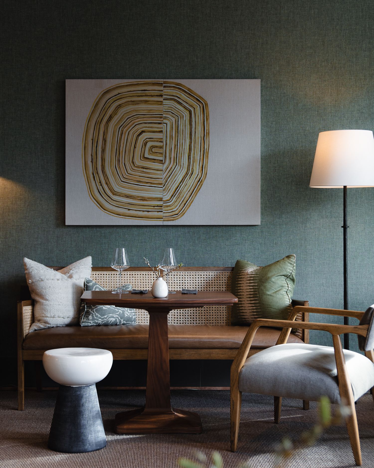 Modern living room with abstract gold spiral artwork, gray walls, wooden bench seating and mid-century modern accent chair.