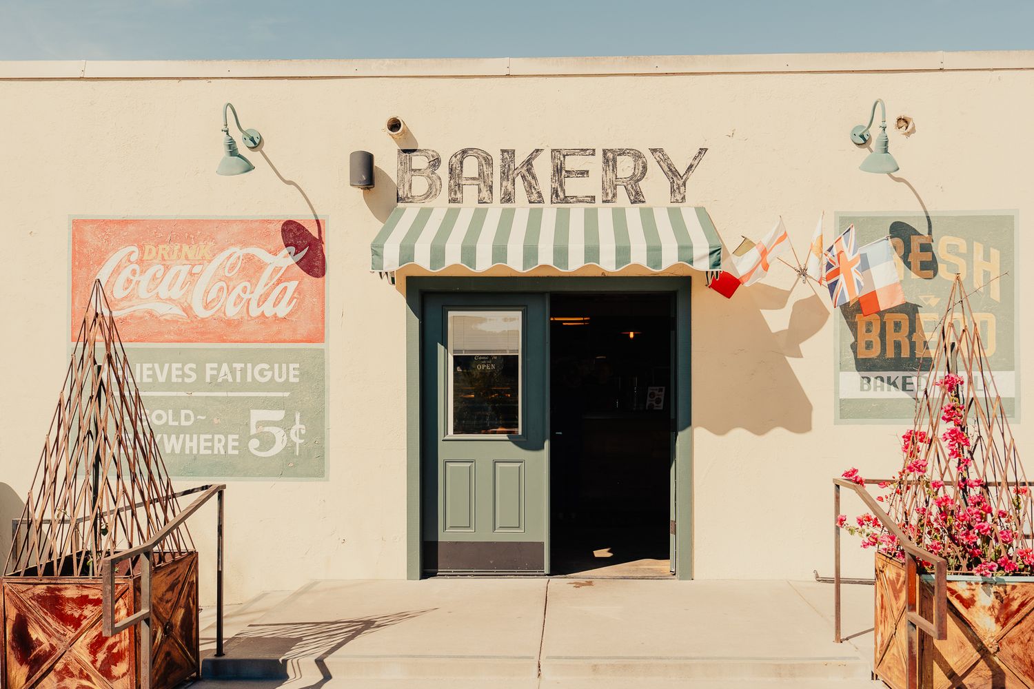 Vintage bakery storefront with striped awning, Coca-Cola signs, and rustic decor in warm sunlight.
