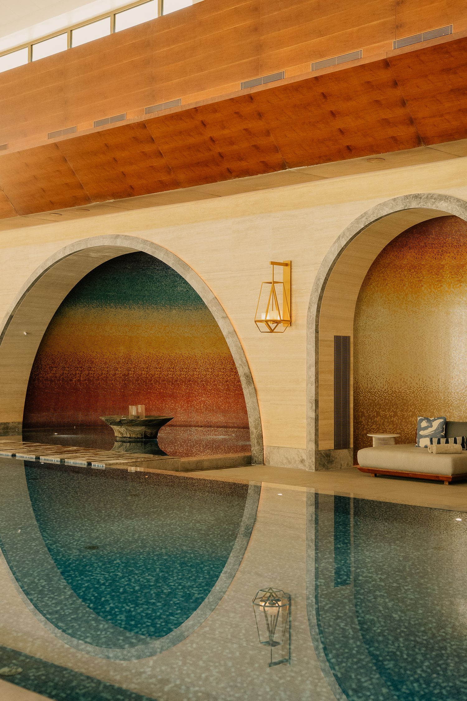 Luxury indoor pool with arched mosaic tile walls, gold lantern sconces, and warm wood ceiling in an elegant spa.