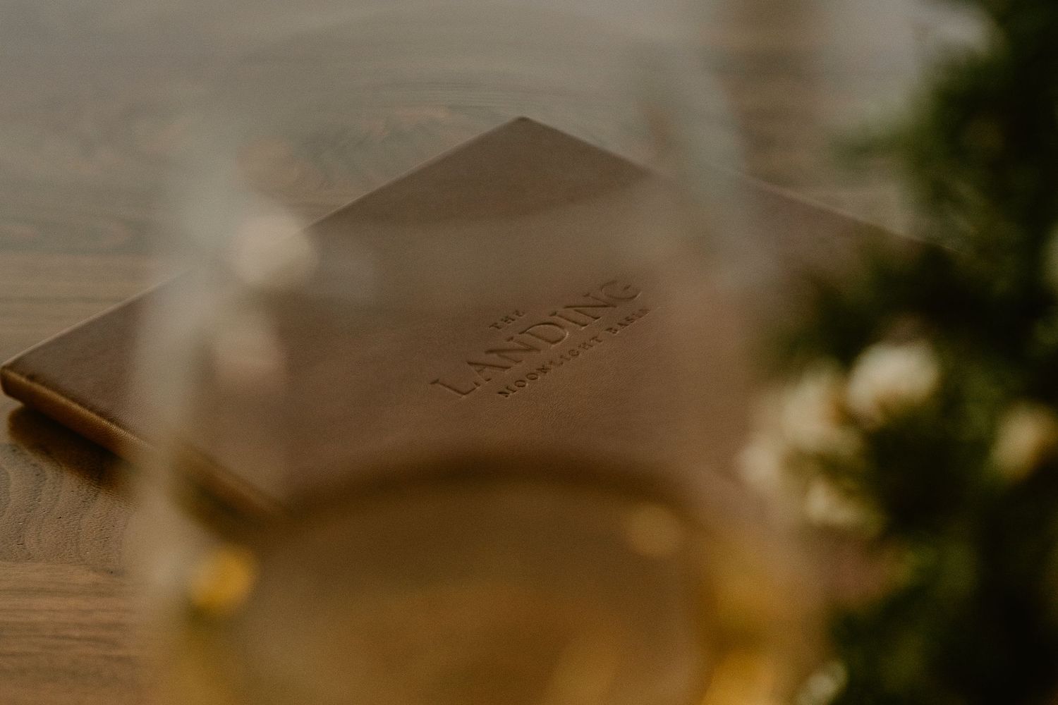 A leather-bound book or journal sits on a wooden surface with soft bokeh lighting effects in the background.