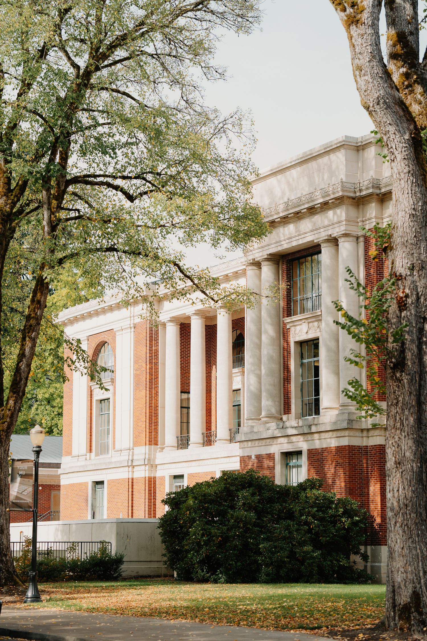 Brick and stone academic building with classical columns and tall windows surrounded by mature trees on a university campus.