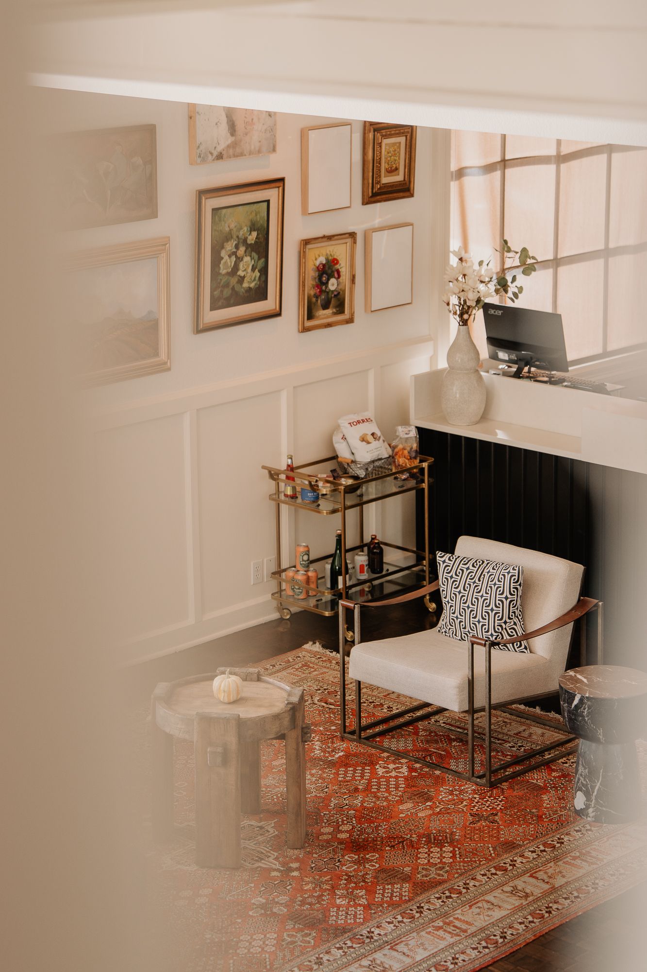 Living room with white wainscoting, ornate oriental rug, and glass coffee table with brass accents.