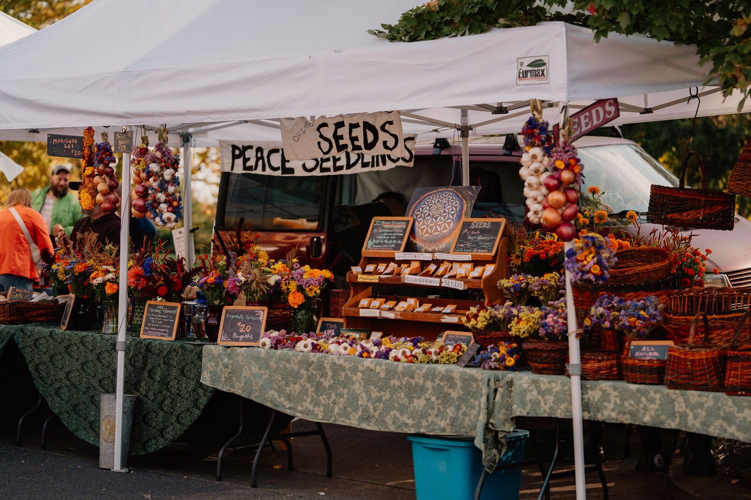 Farmers market vendor booth displaying colorful peeks snacks and produce under white canopy tent.