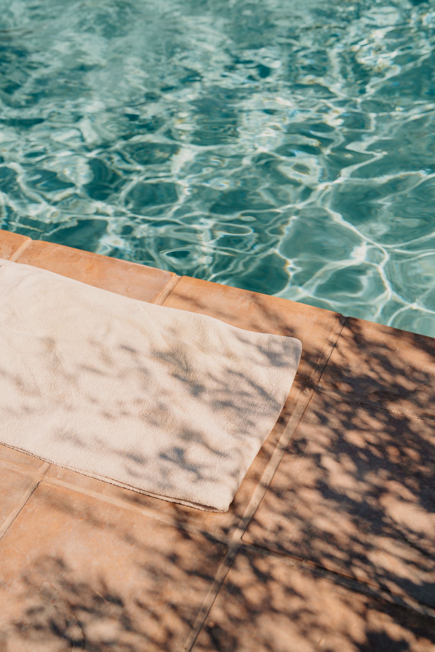 Rippling turquoise pool water meets a beige towel on the edge, creating a serene summer scene.