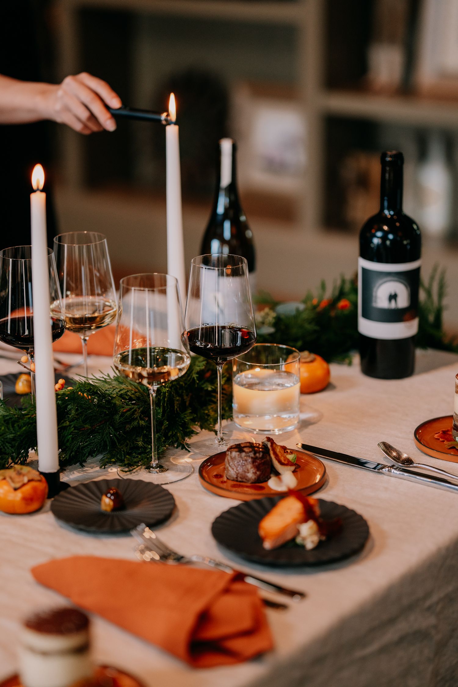 Elegant table setting with wine glasses, candles, and persimmons arranged on white tablecloth for intimate dinner party.