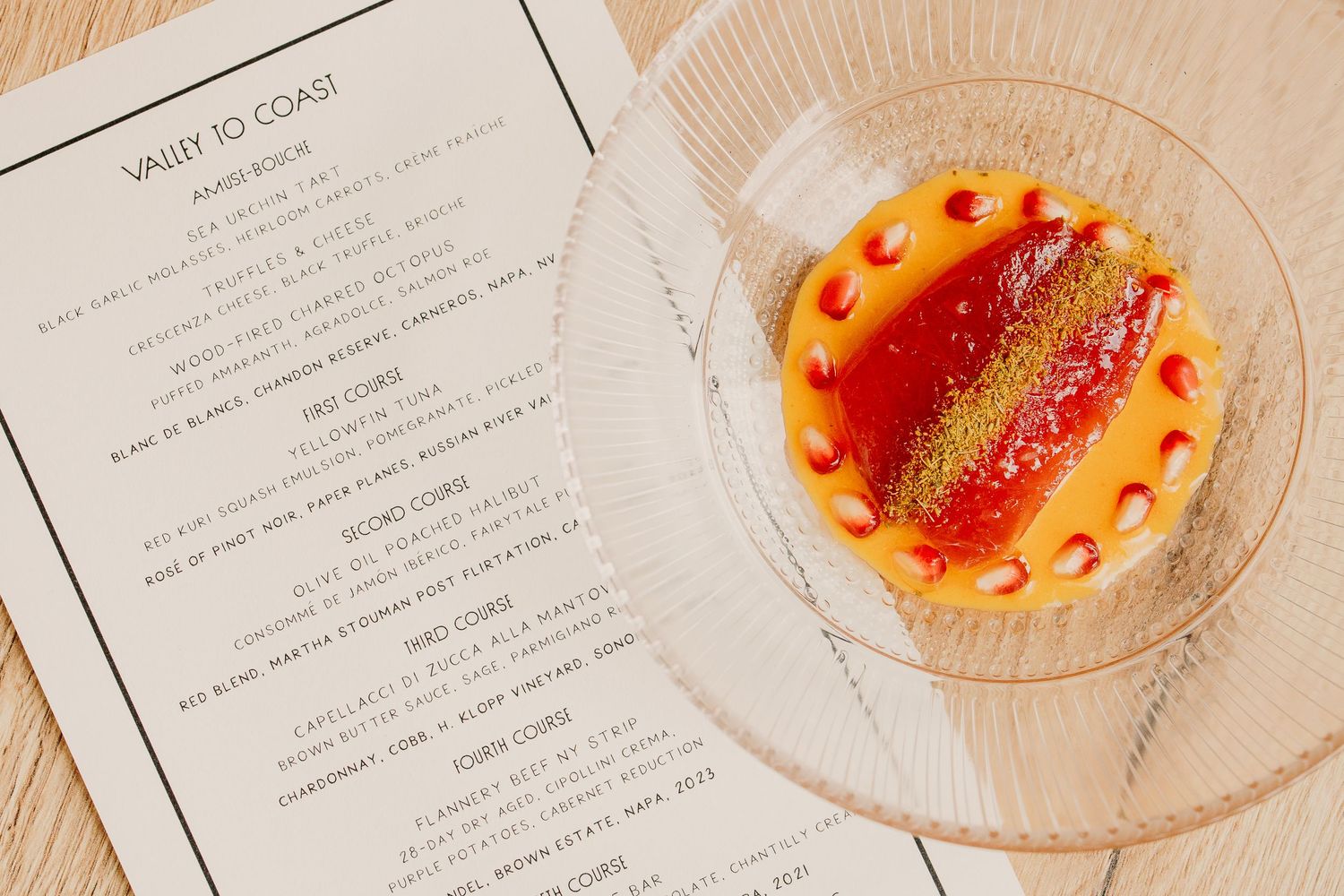 Restaurant menu and cocktail glass with orange garnish displayed on white tablecloth.