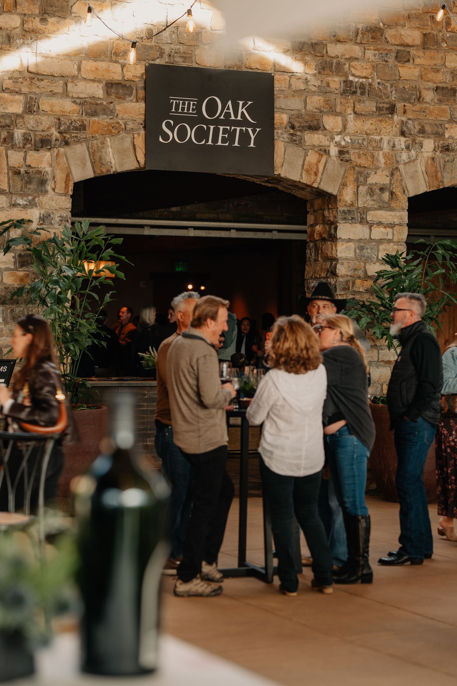 Guests socializing under The Oak Society sign at Silver Oak winerys stone-walled tasting room.
