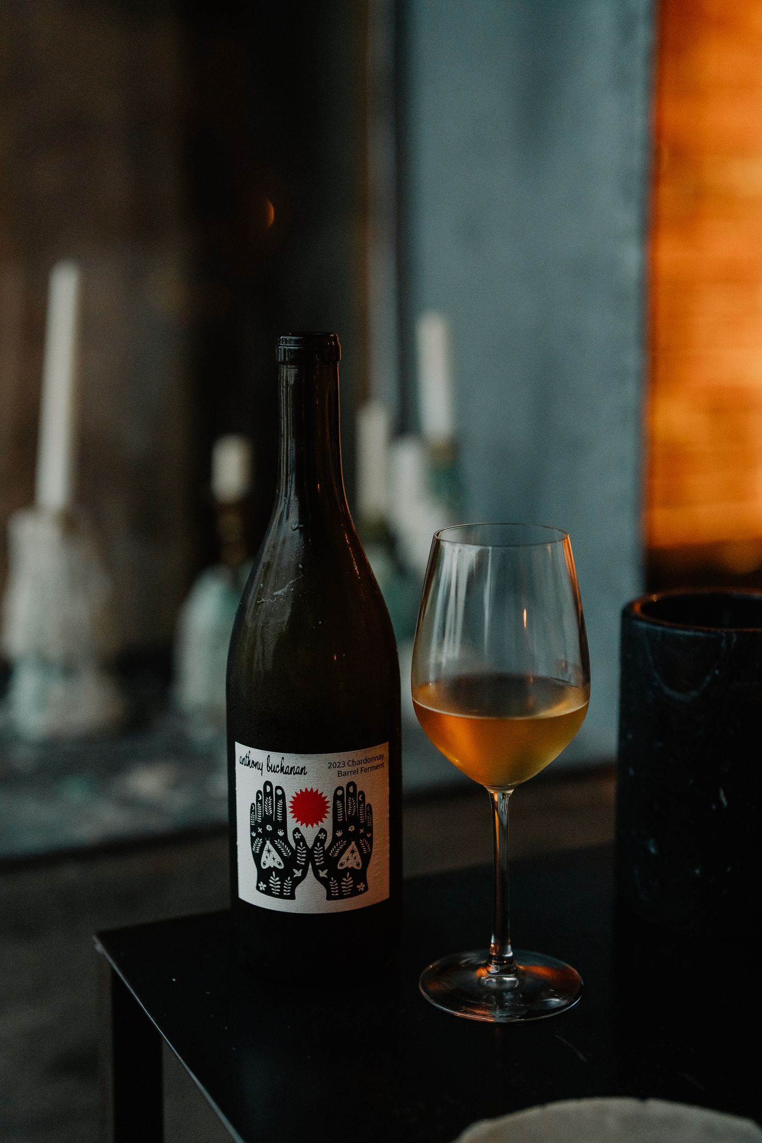 Glass of amber beer sits next to dark bottled craft brews on moody bar counter with warm lighting.