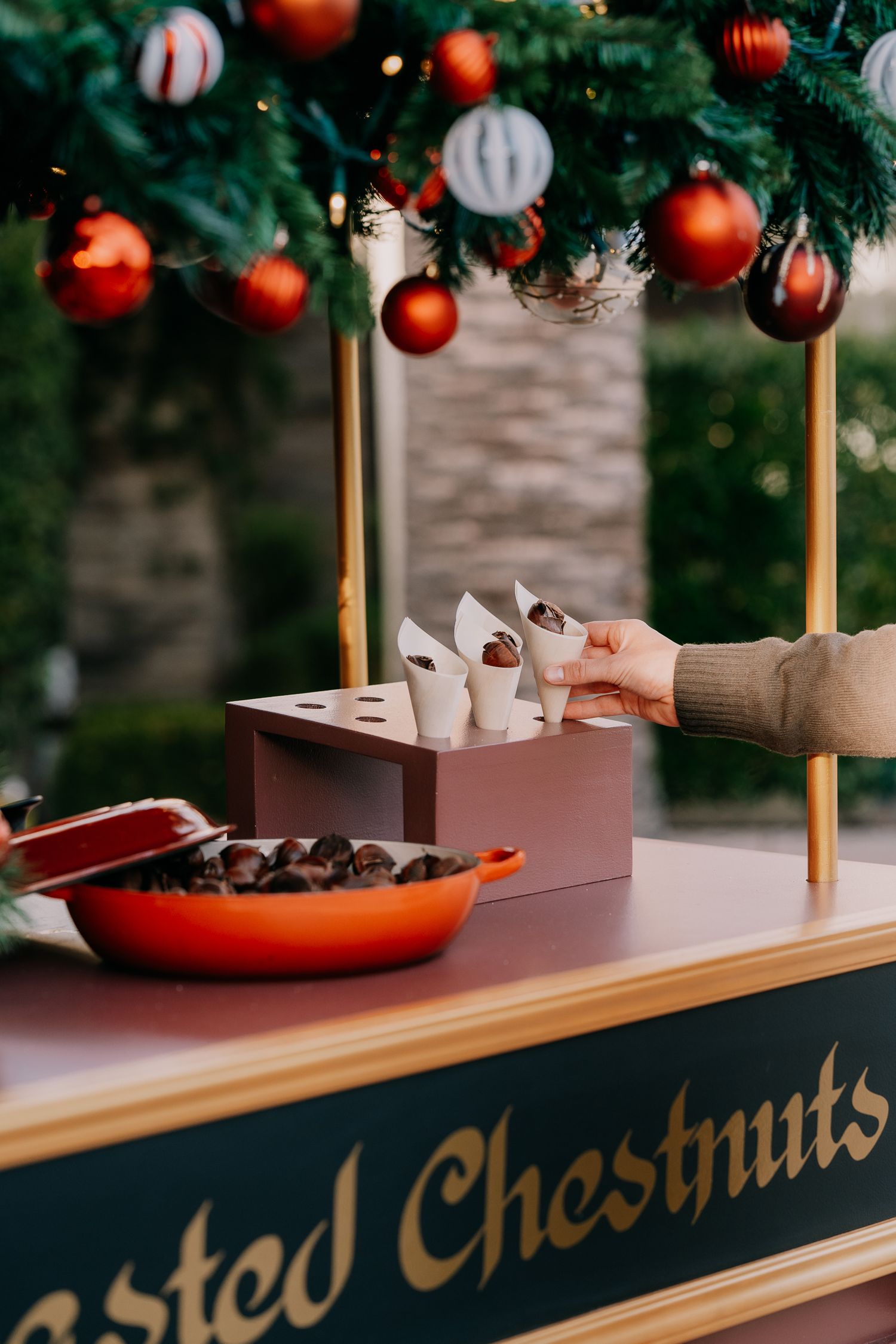 Christmas ornaments hang above a wooden counter displaying chocolate chestnuts and small cups for holiday treats.
