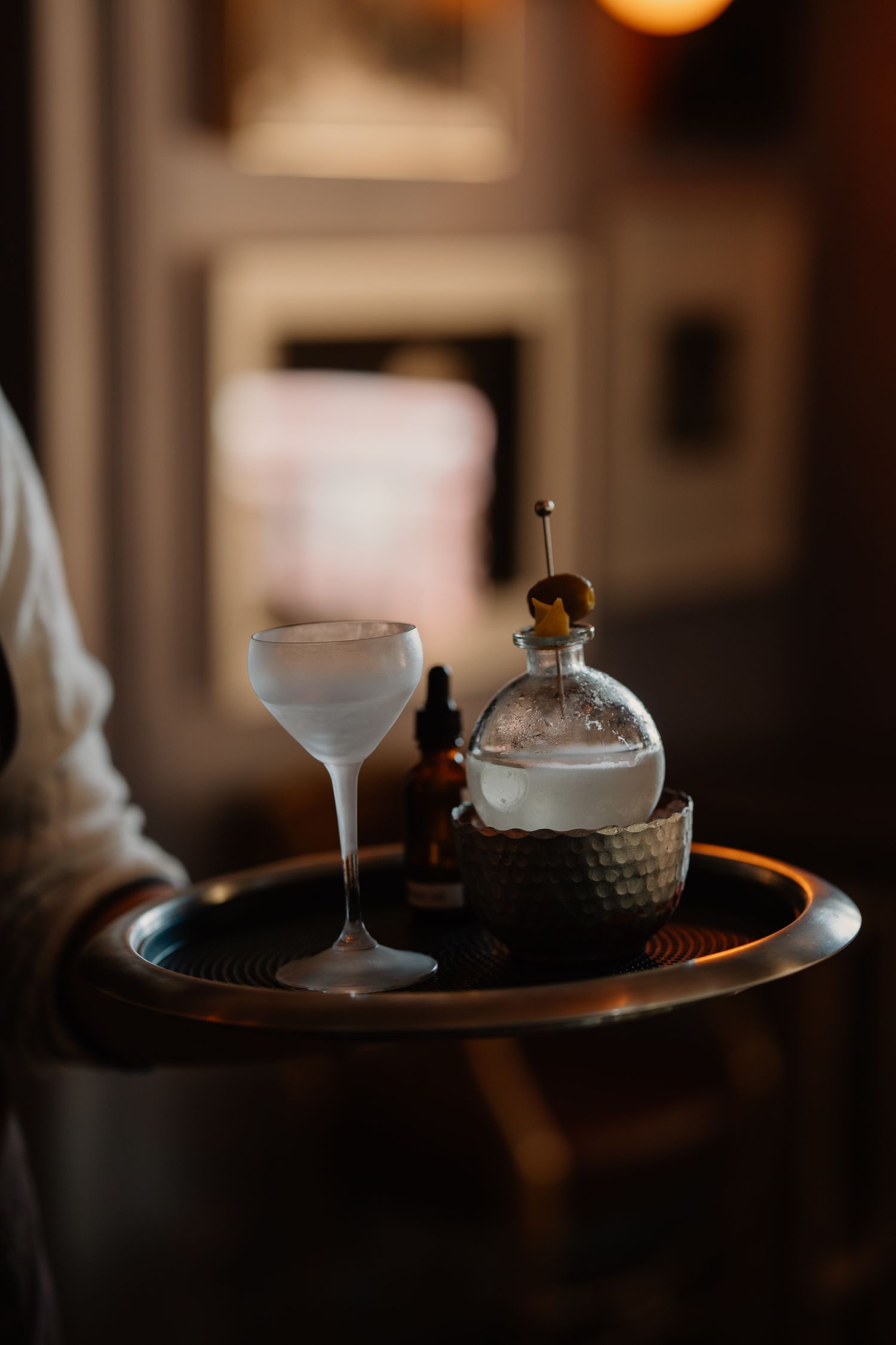 Moody cocktail bar setting with glowing amber lights illuminating elegant glassware on a dark wooden surface.