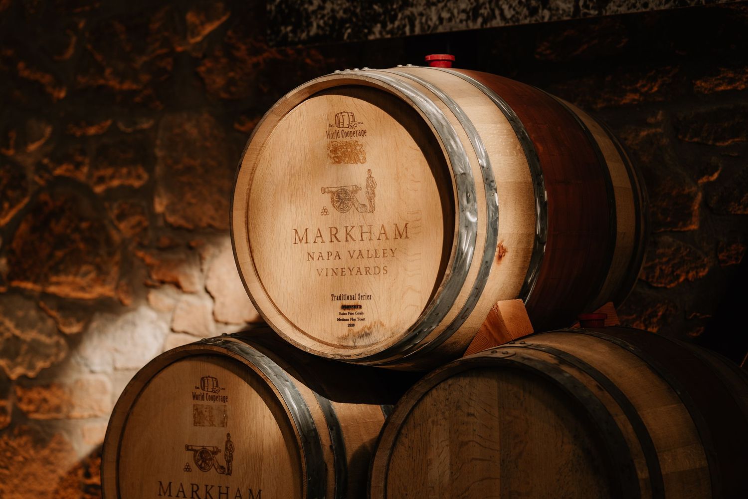 Aged oak wine barrels stacked in a dimly lit cellar at Markham Napa Valley Vineyards.