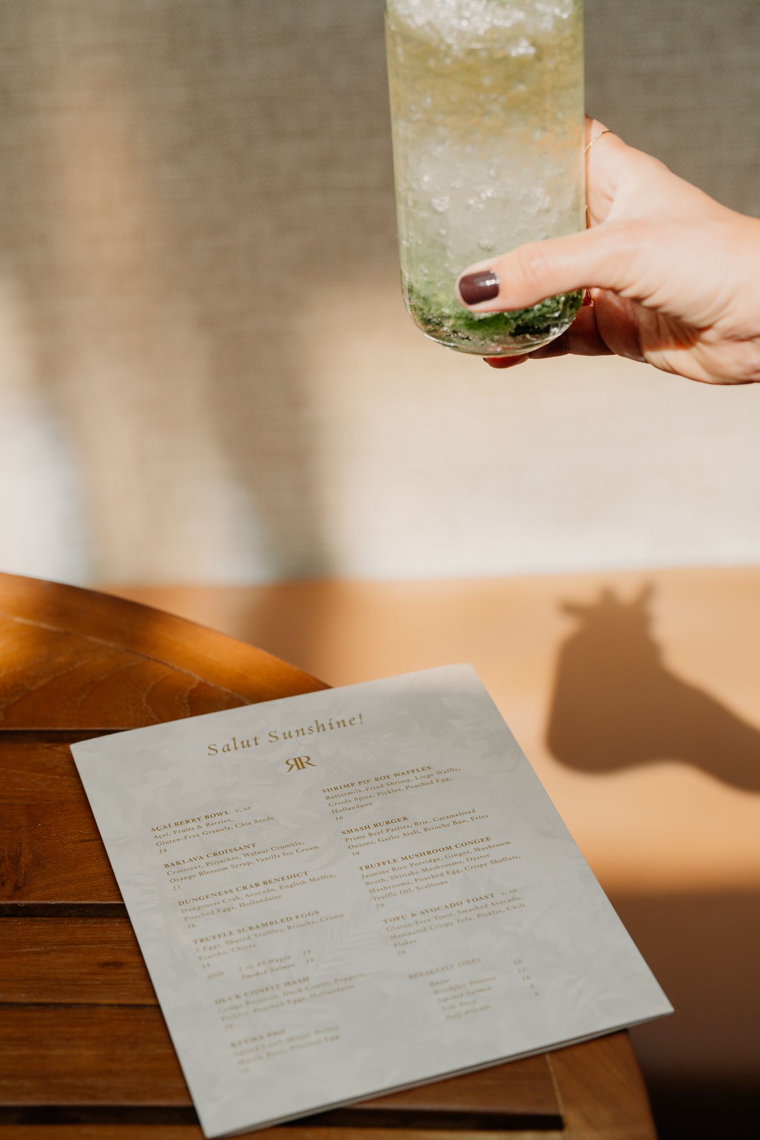 A close-up of a drink menu and cocktail with shadow casting on wooden table surface.