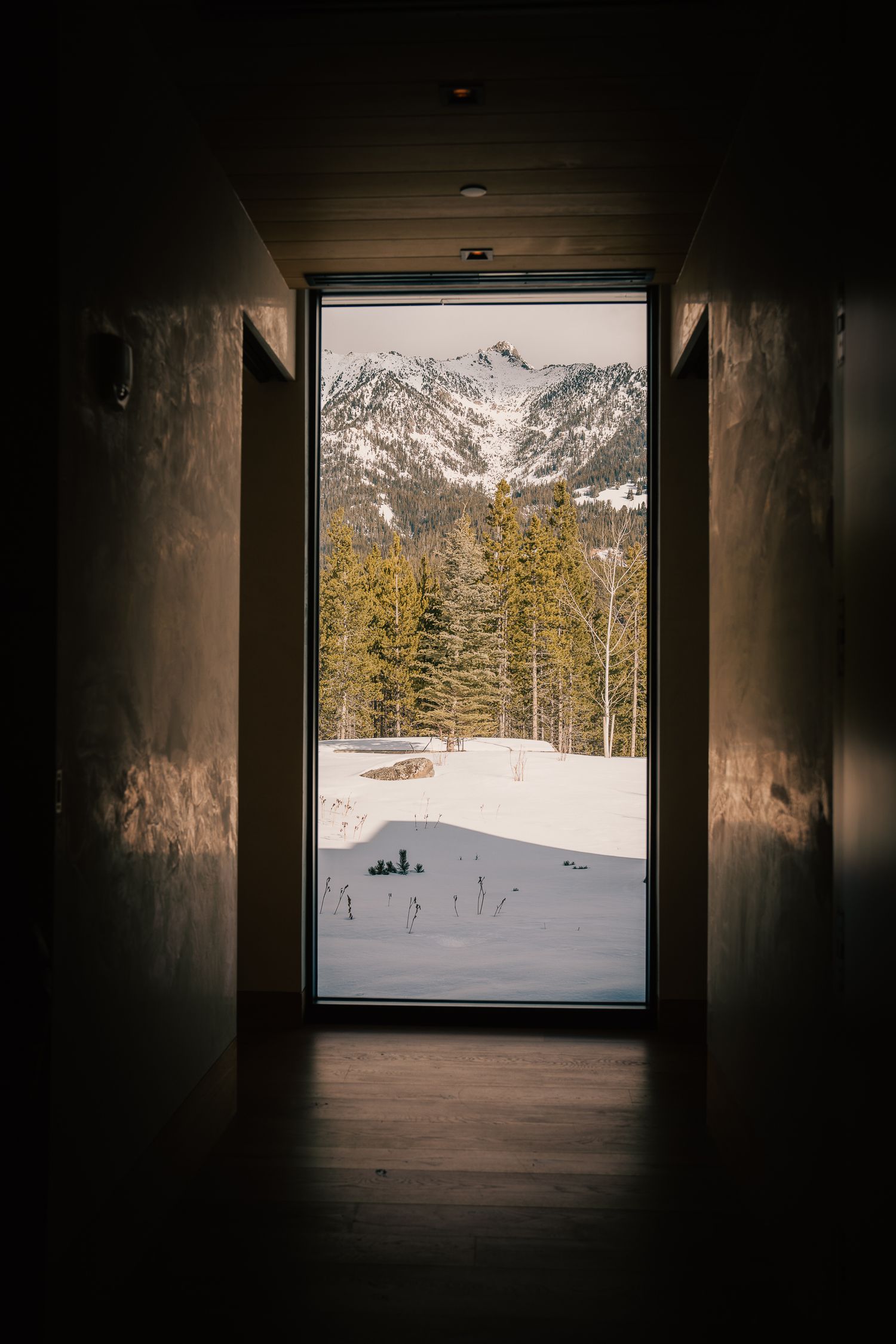 Snow-covered mountain landscape framed through a dark tunnel or hallway window.
