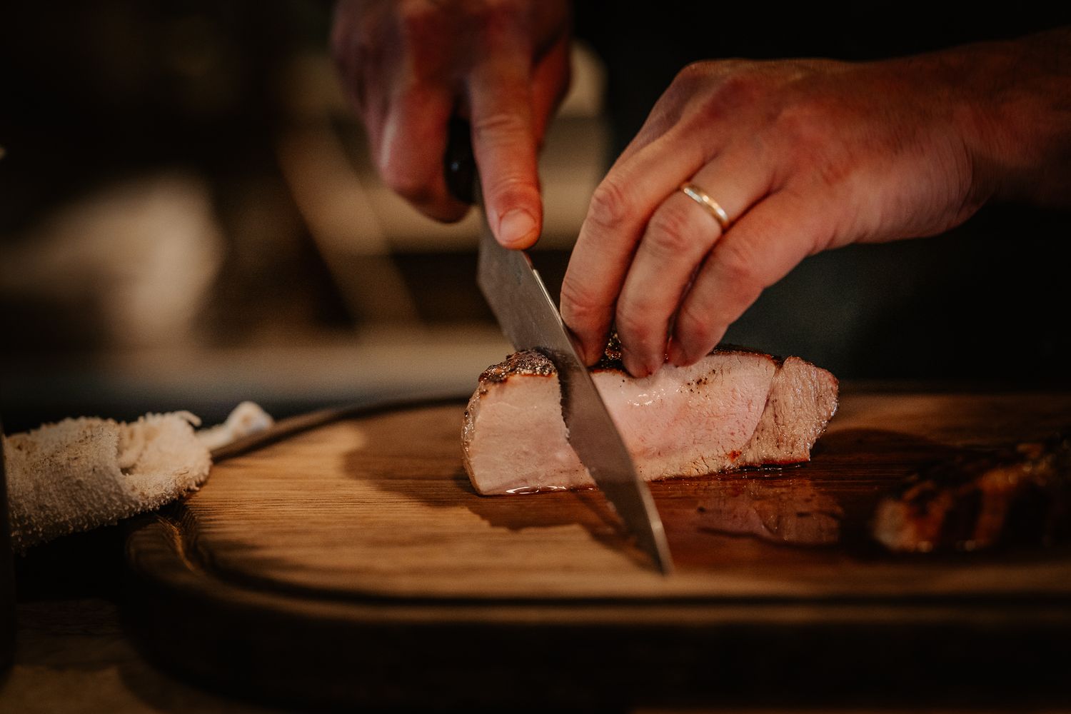 Hands slicing roasted pork on a wooden cutting board with a sharp knife, revealing juicy pink meat.