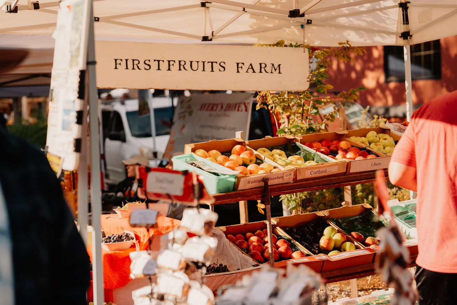 Fresh produce display at FirstFruits Farm vendor booth with colorful fruits and vegetables arranged at farmers market.