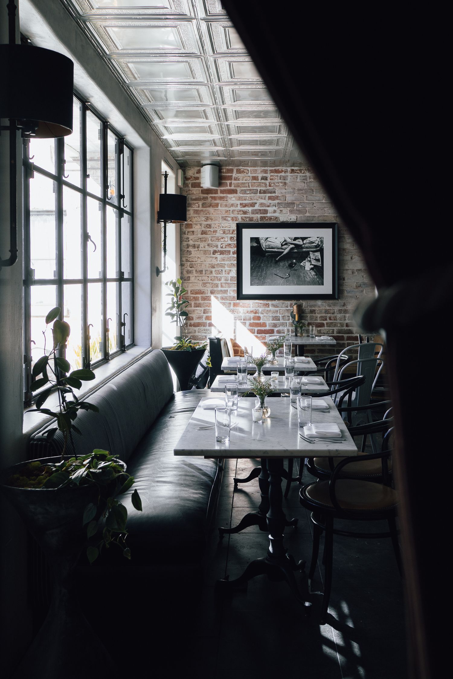 Elegant restaurant interior with exposed brick walls, leather banquettes, and dramatic lighting through large windows.