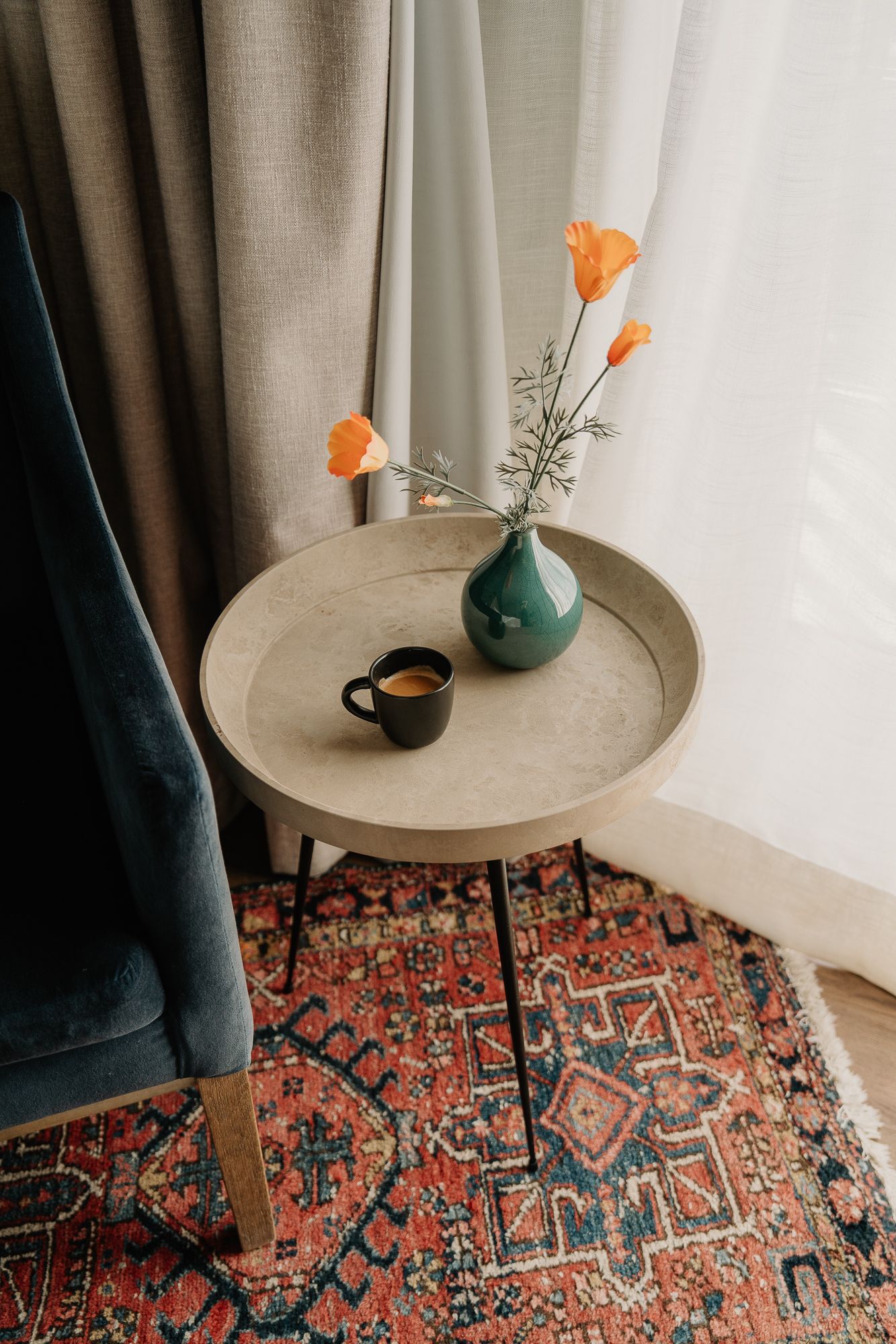Modern side table with turquoise vase holding orange flowers against a patterned oriental rug.