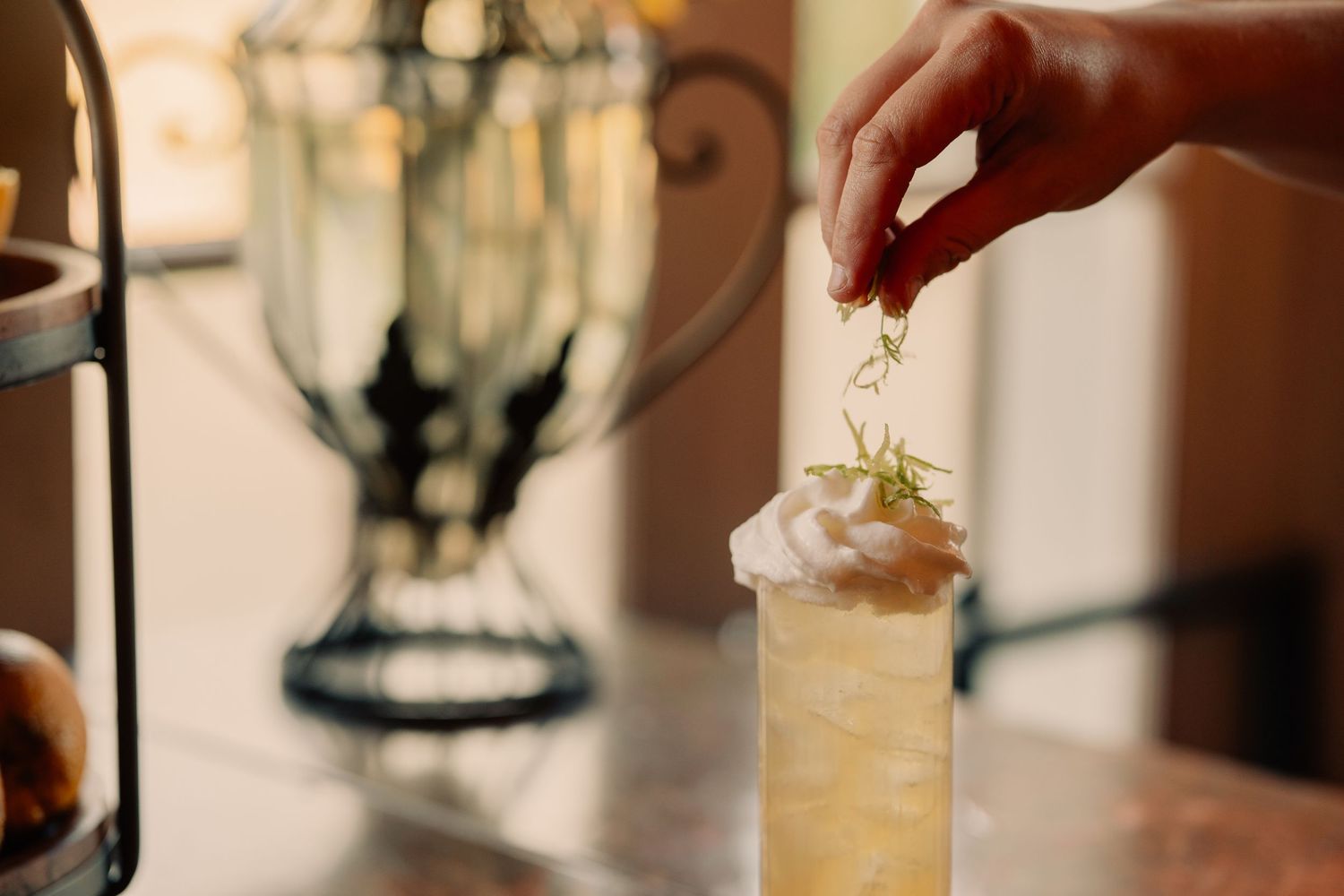 Hands pouring and mixing cocktails at an upscale bar with professional bartending equipment and soft lighting.