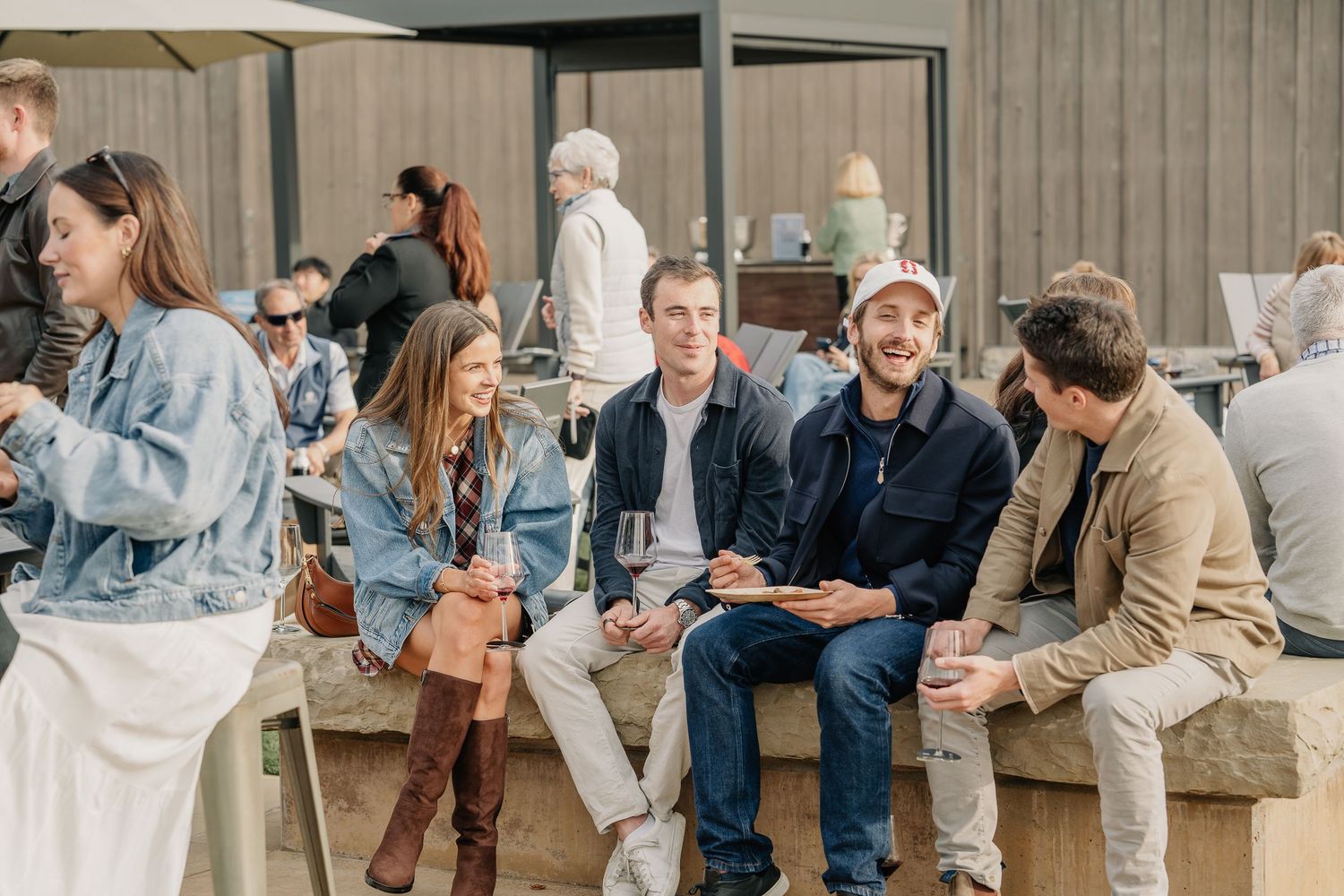 Group of young adults socializing outdoors at a casual gathering, sitting on stone benches in a modern courtyard.