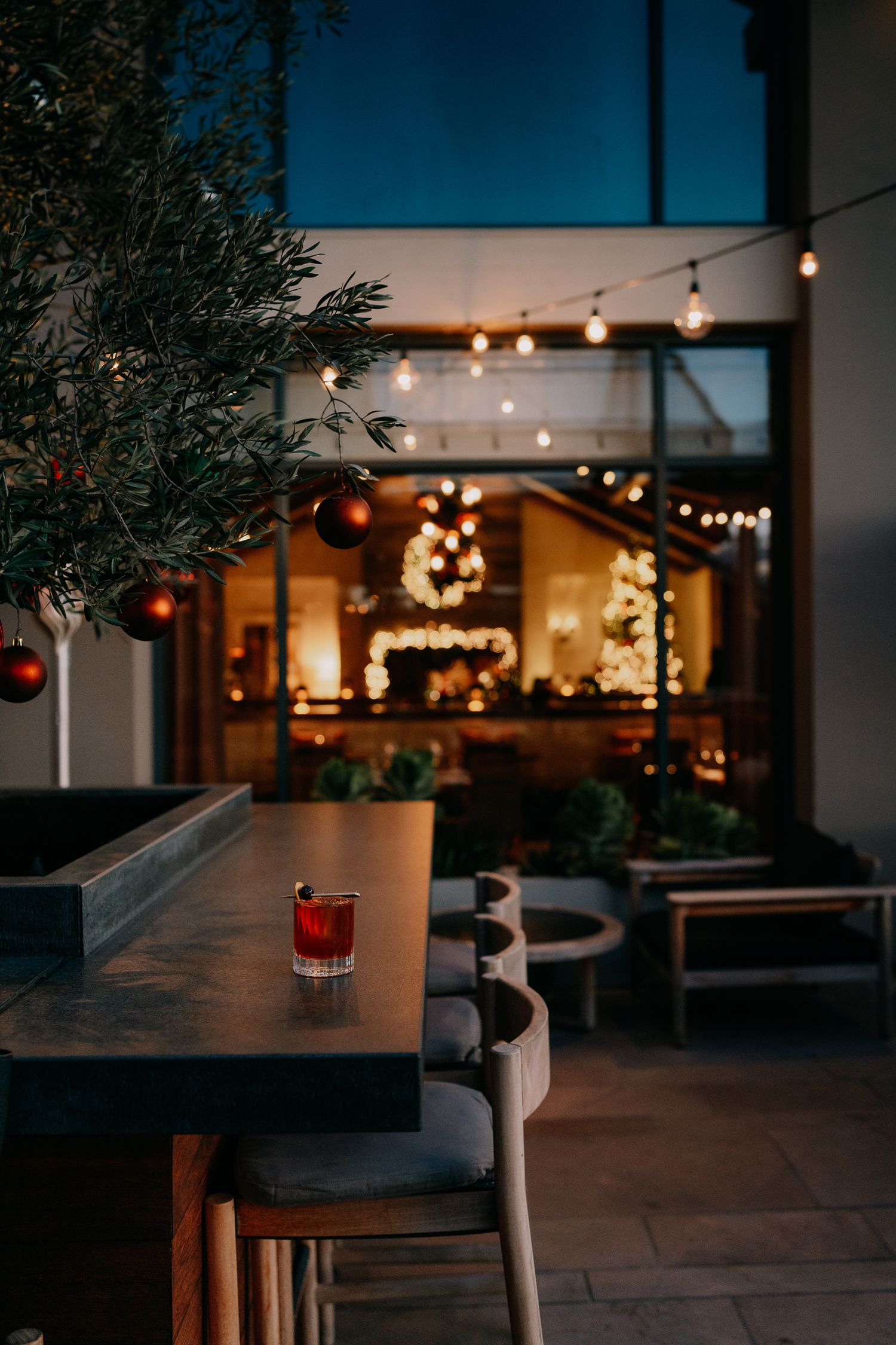 String lights illuminate a cozy outdoor patio seating area at dusk with glowing red lanterns and modern furniture.