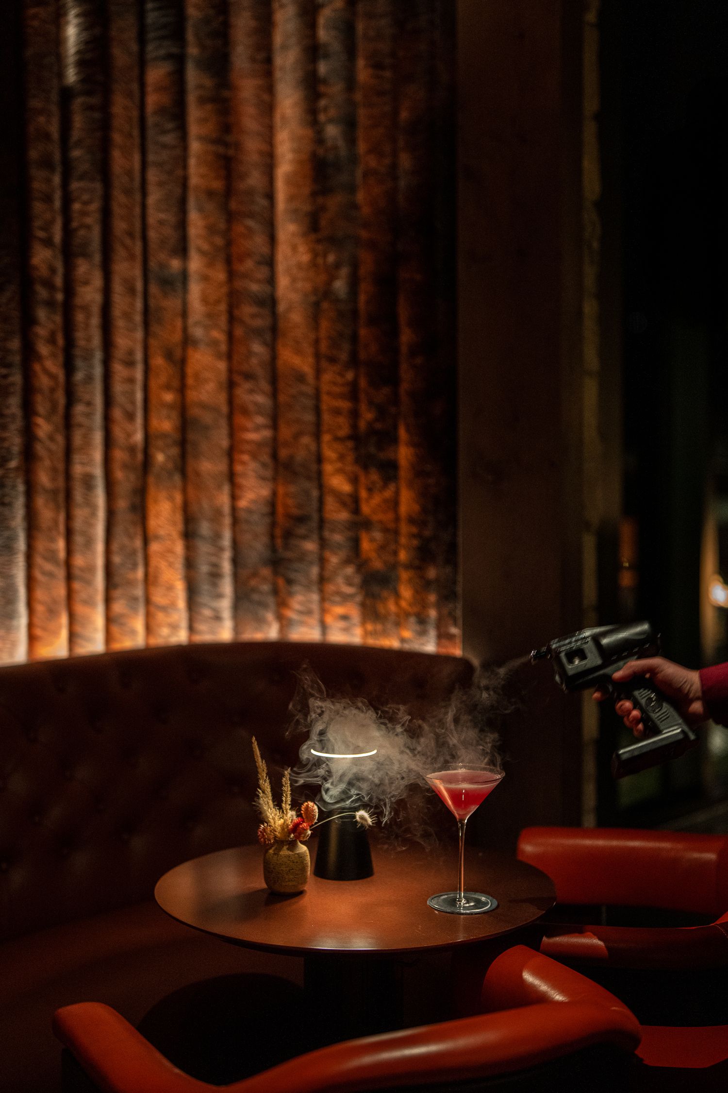 Dimly lit cocktail lounge with moody red lighting and backlit textured wall panels creating an intimate atmosphere.