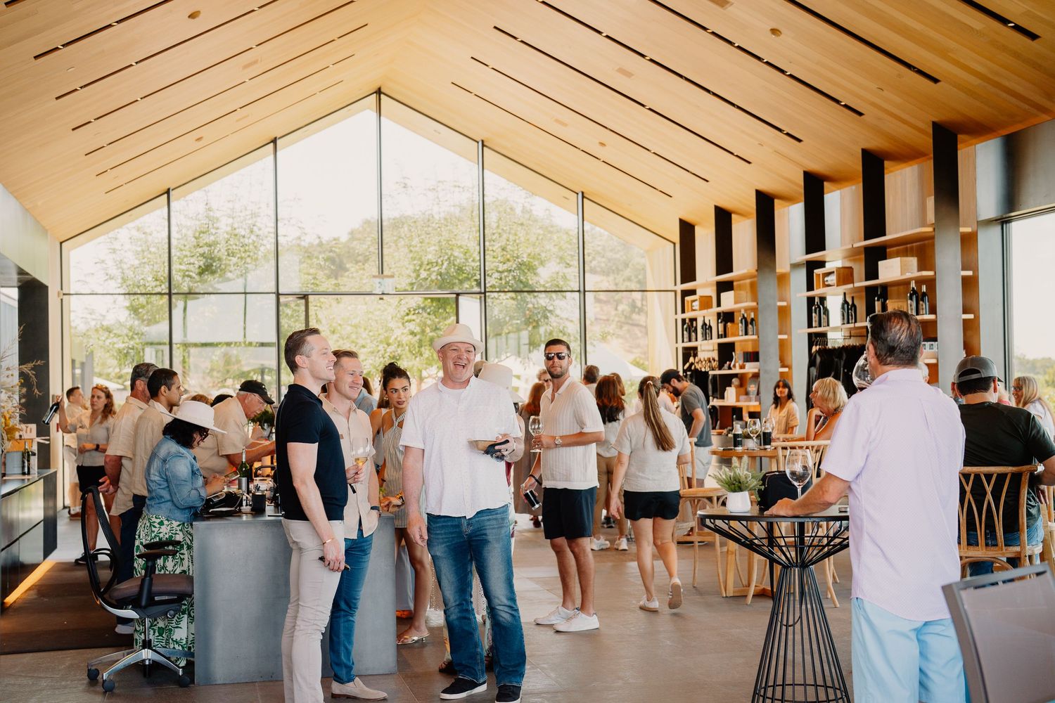 Guests mingle in a modern winery tasting room with wood-paneled ceilings and large windows.
