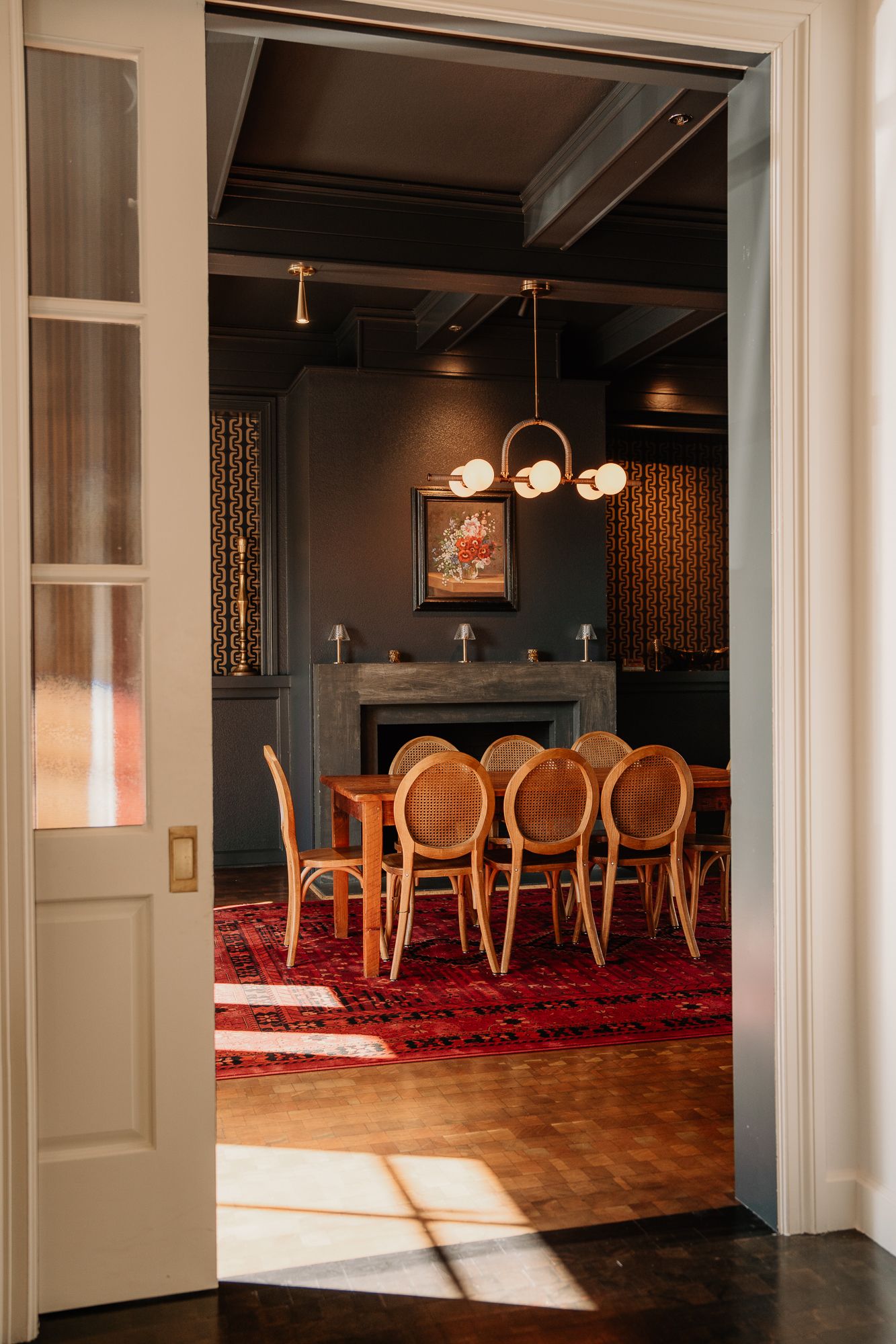 Elegant dining room interior with wooden chairs and red carpet featuring modern pendant lighting and white walls.